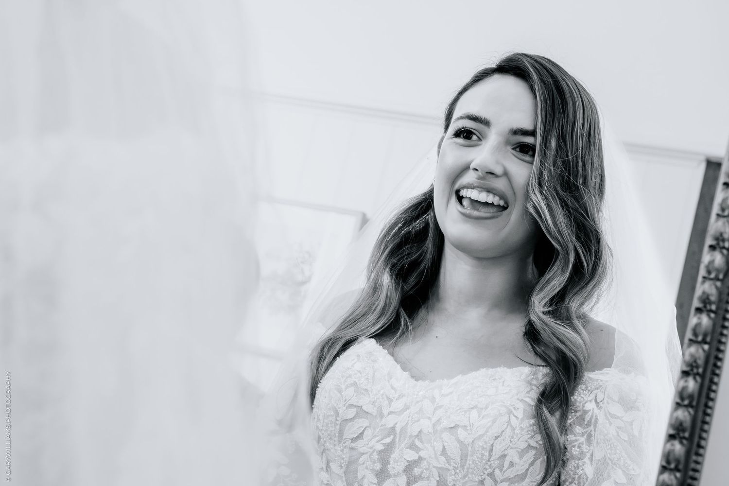 Black and white photo of a smiling bride in a lace wedding dress with flowing hair on her wedding day.