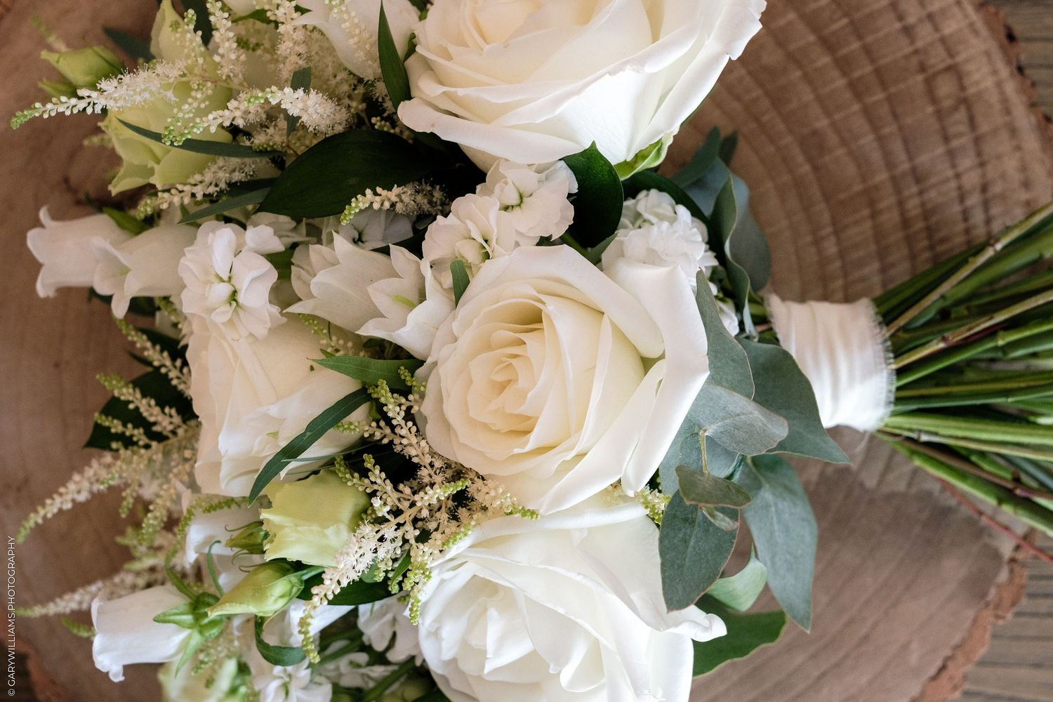 Elegant white wedding bouquet featuring roses, astilbe, and greenery arranged in a wicker basket.