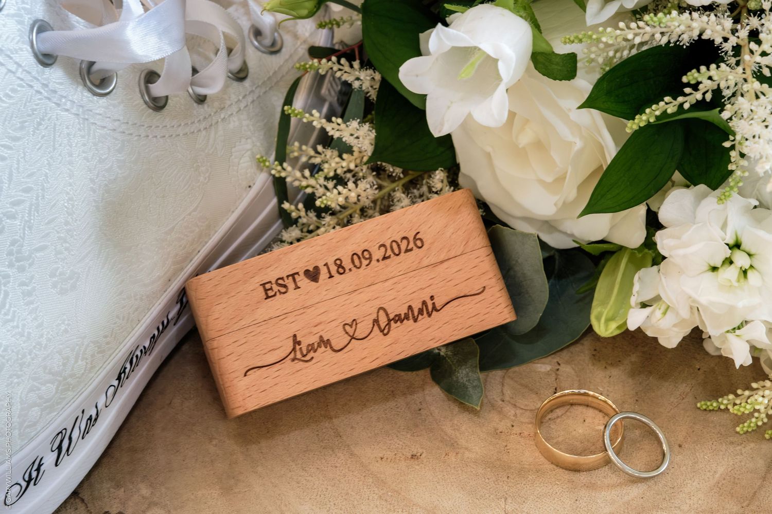 Wooden wedding keepsake box engraved with EST 18.09.2026 beside white floral bouquet and gold wedding rings.