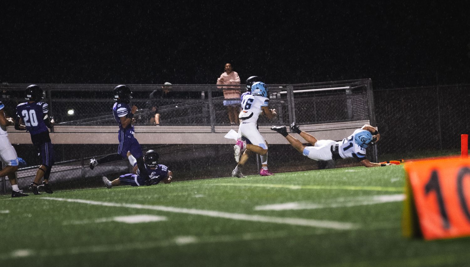 Football players competing near the goal during a nighttime match under stadium lights.
