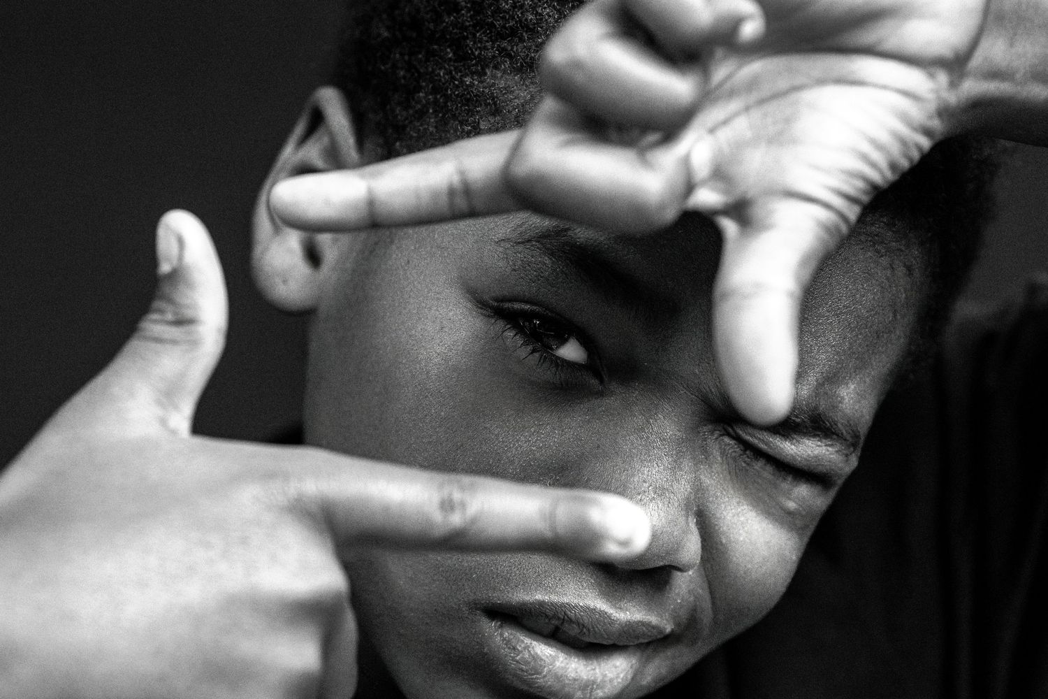 Black and white portrait of a young man framing his eye with fingers in a creative photography pose.