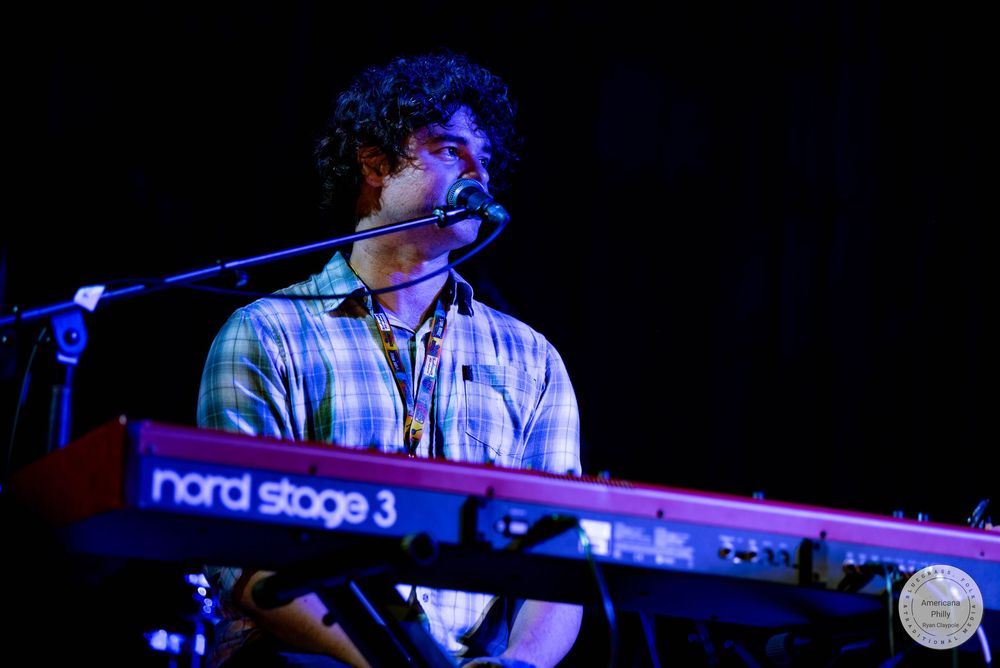 Musician playing a red Nord Stage 3 keyboard on stage while singing into a microphone at a live concert.