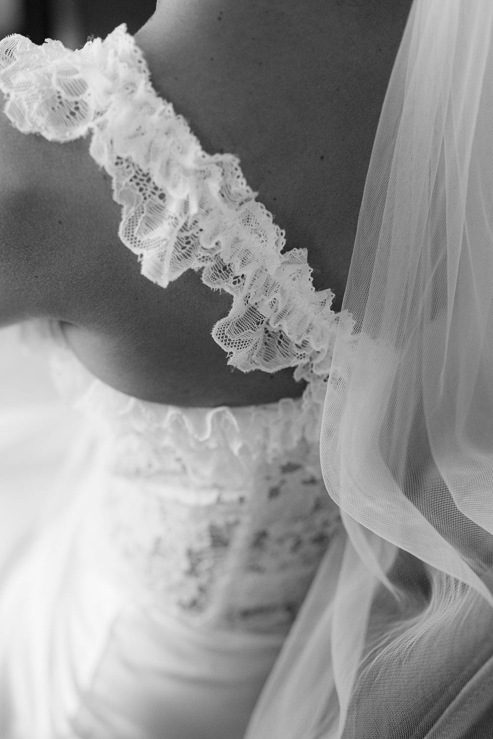 Black and white close-up of a bride in a lace wedding dress with a ruffled garter and flowing veil.