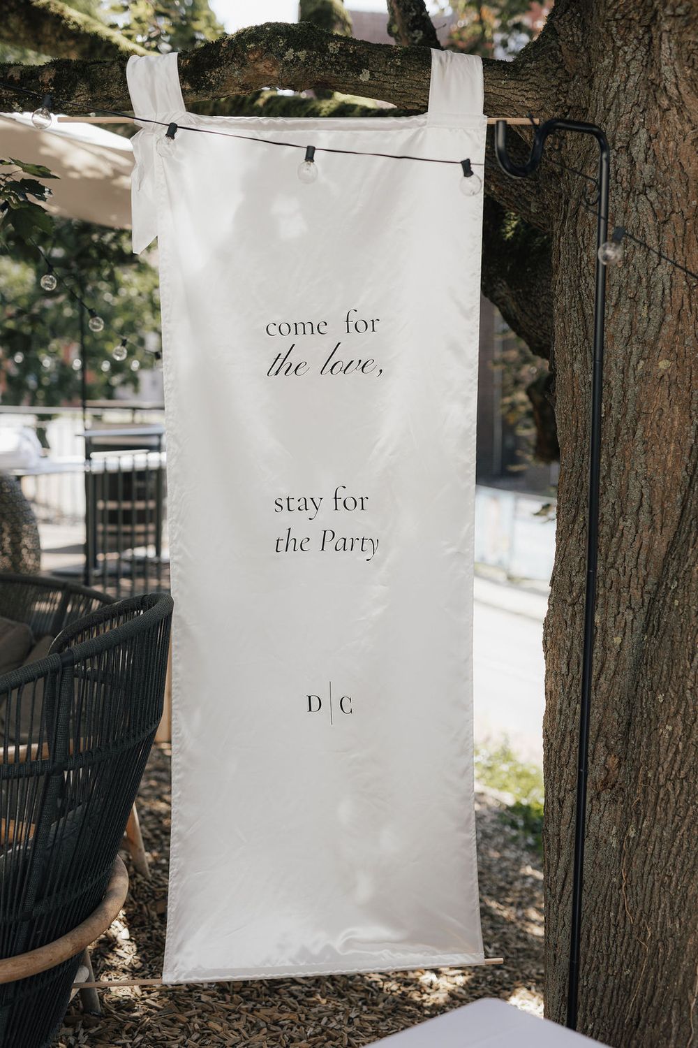 White wedding banner hung outdoors reading come for the love, stay for the Party with monogram D|C.