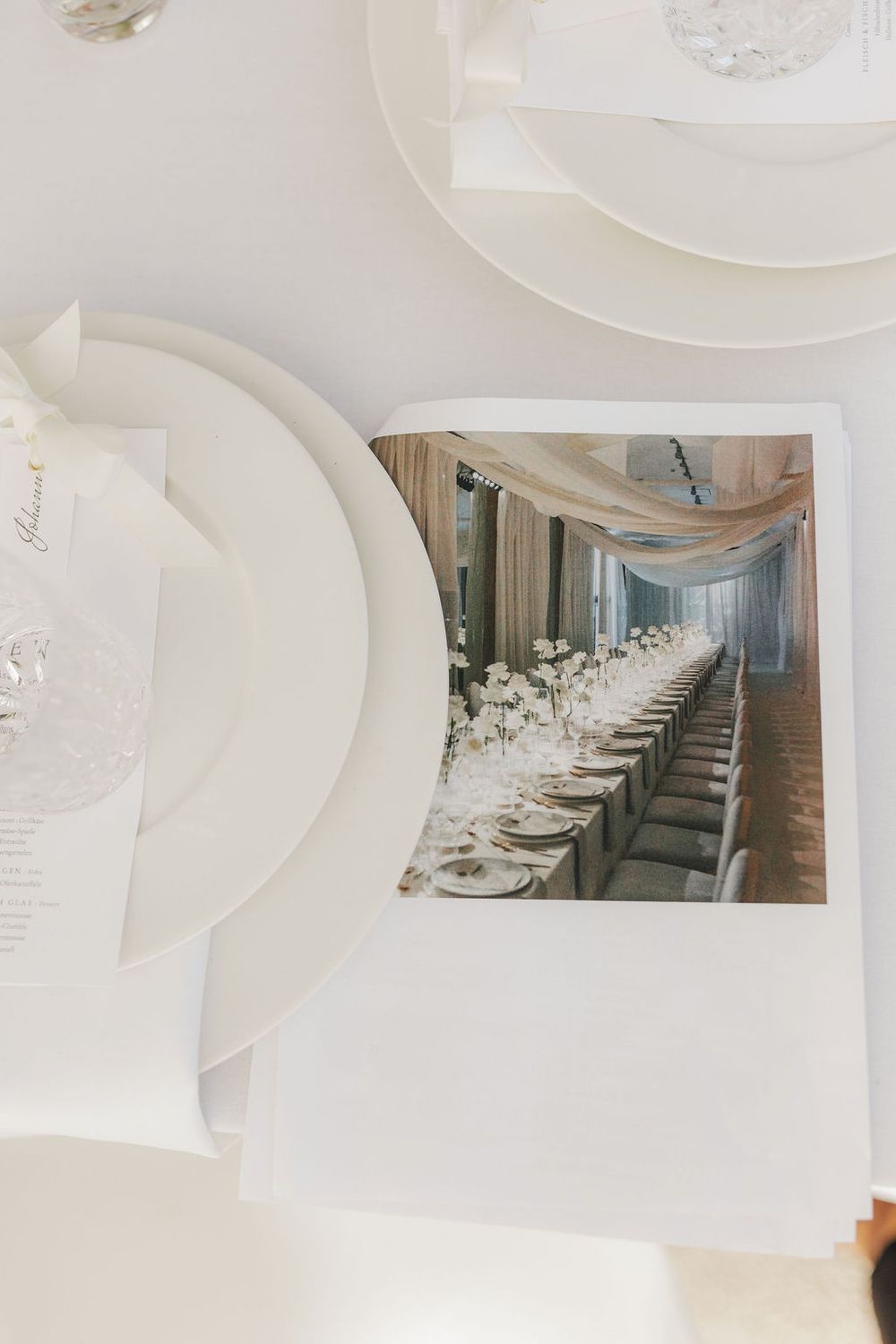 Elegant wedding table setting with white plates, menu cards, and a photo of a long reception dinner table with floral centerpieces.