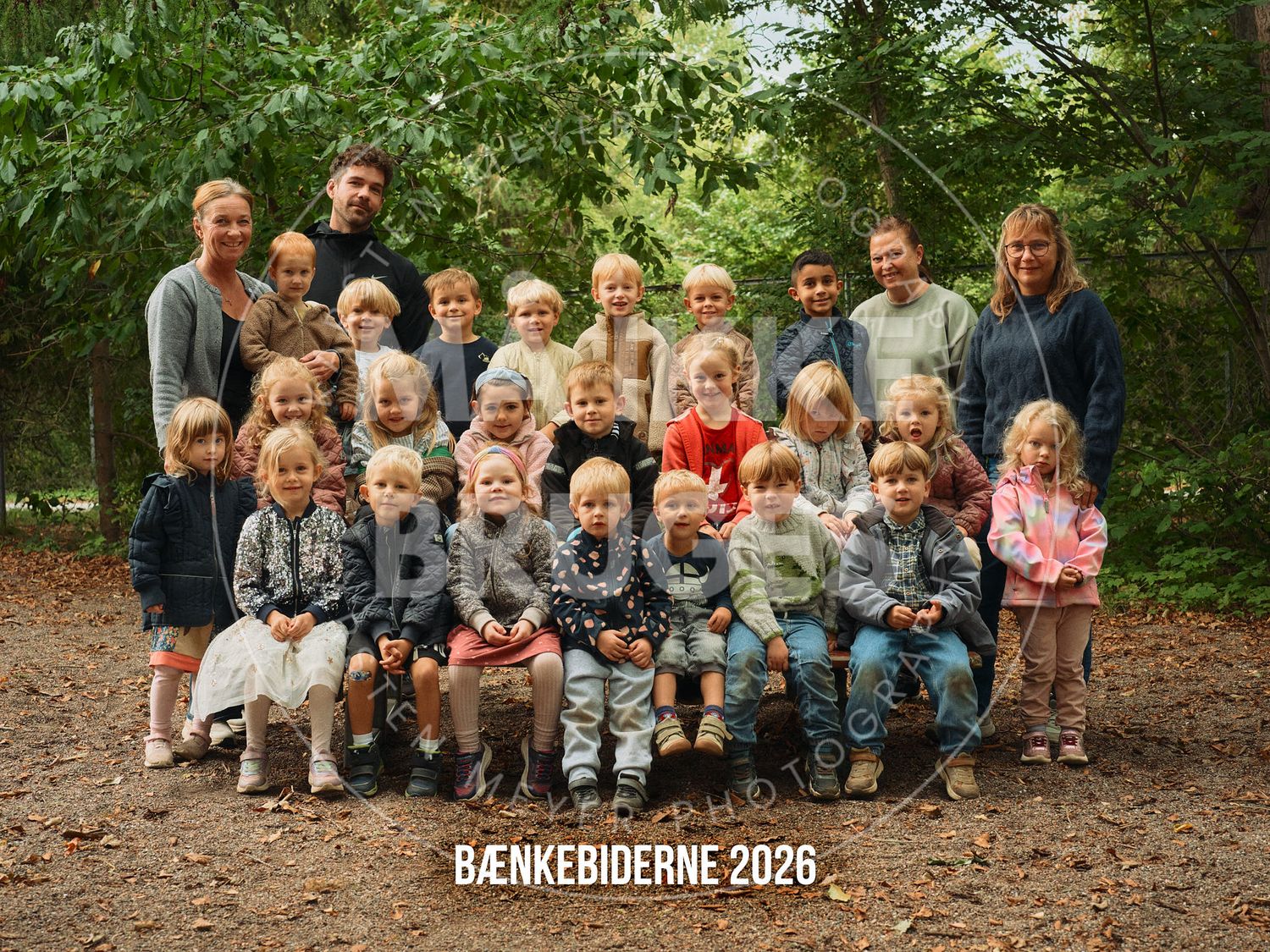 Group photo of children and teachers in a forest setting, labeled Bænkebiderne 2026.