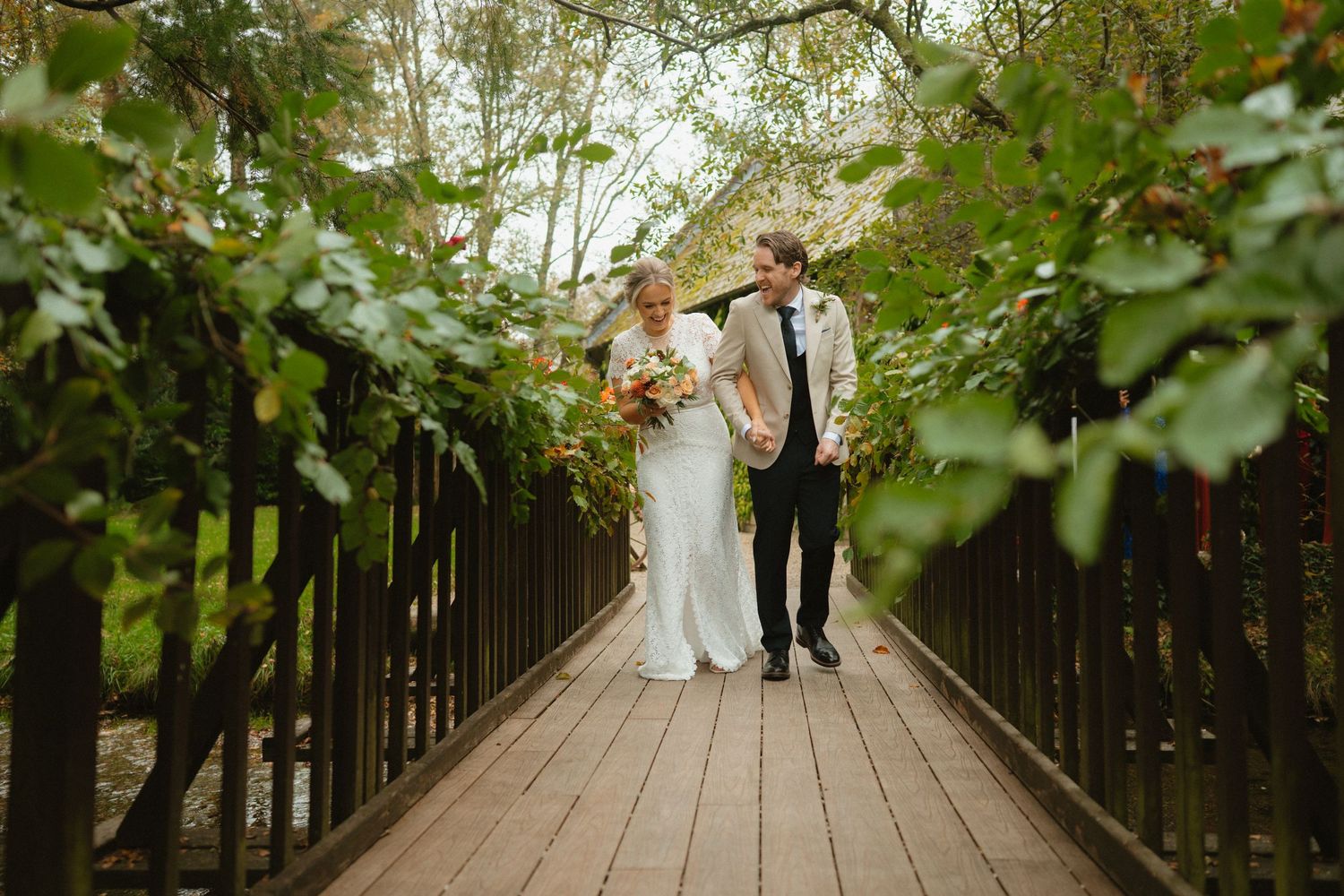 Bride and groom walking across the leafy wooden bridge at BrookLodge and Macreddin Village.