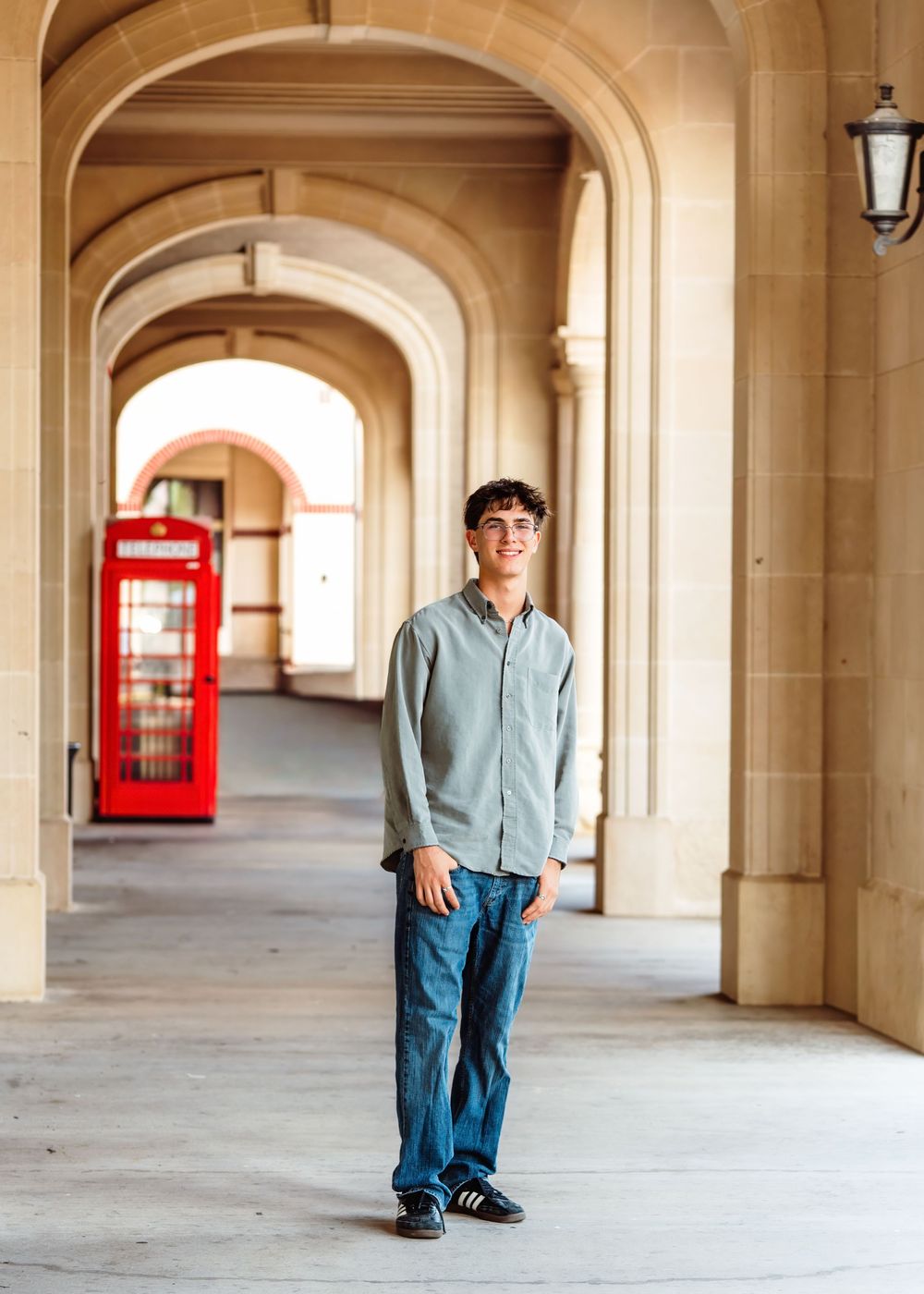 Young man smiling in a stone archway corridor with a red British phone booth in the background.