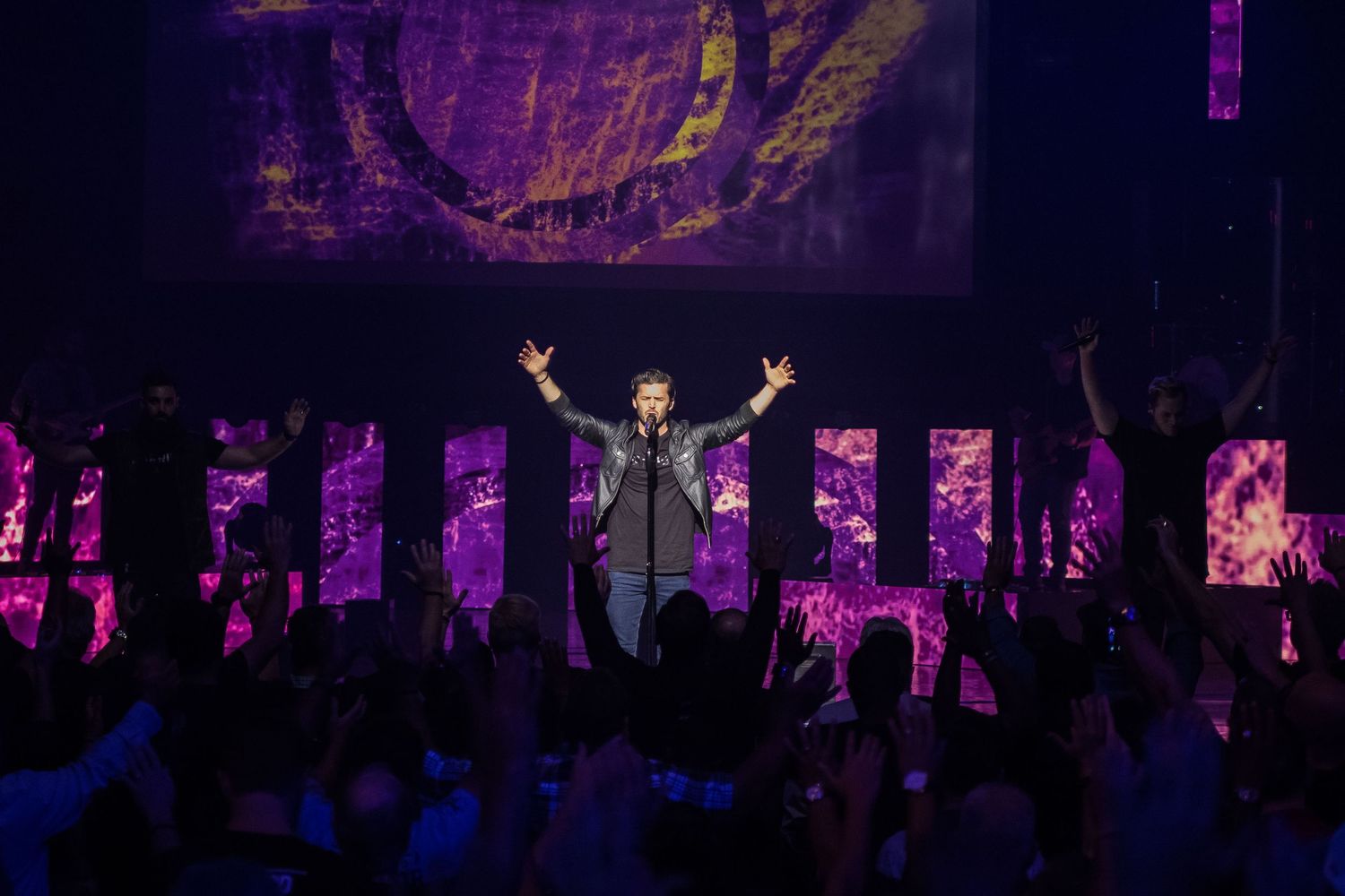 Concert venue with purple lighting and silhouetted crowd enjoying performance.