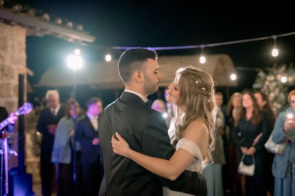 Couple shares first dance at outdoor wedding reception under string lights with guests watching.