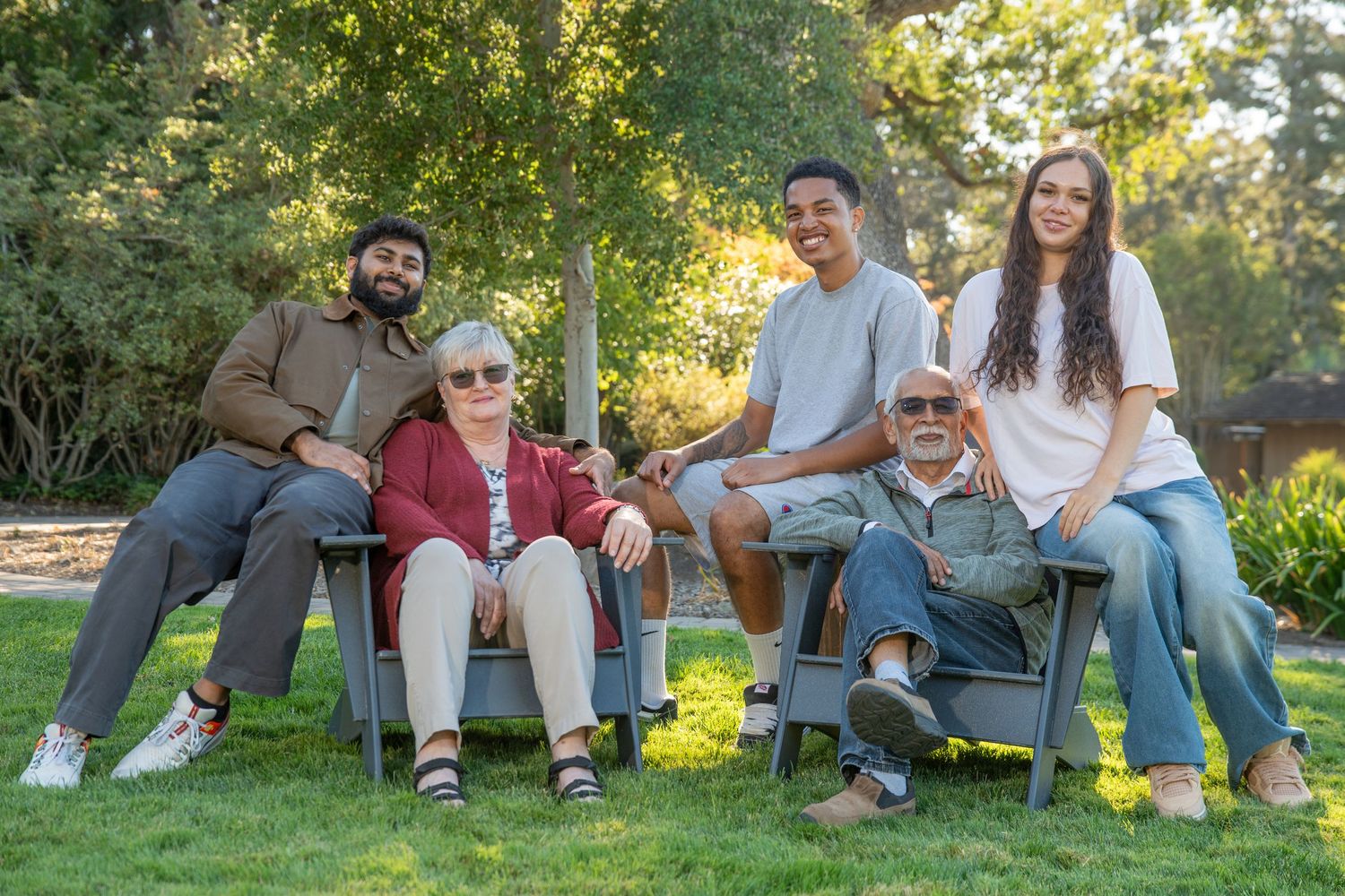 Multi-generational family of five smiling together outdoors in a lush green park on a sunny day.
