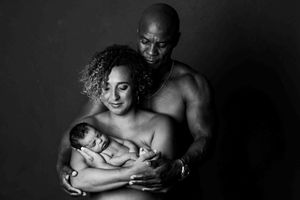 Black and white portrait of parents tenderly holding their newborn baby in a studio setting.