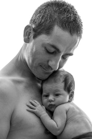 Black and white photo of a shirtless father tenderly holding his newborn baby against his chest.