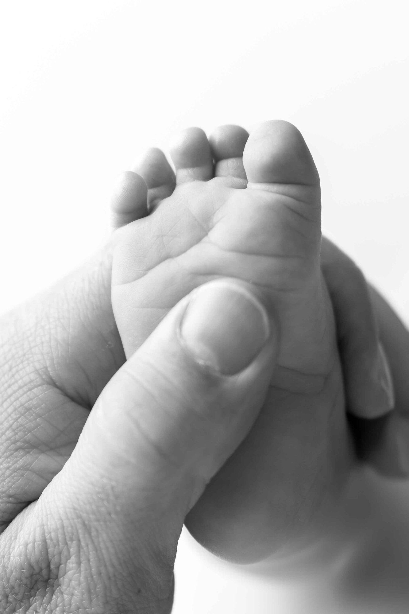 Black and white close-up of an adult hand gently holding a tiny newborn baby foot, symbolizing love and new life.