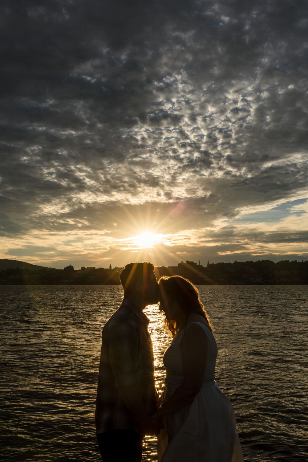 Romantic couple silhouetted against a stunning golden sunset over a lake with dramatic cloudy sky.