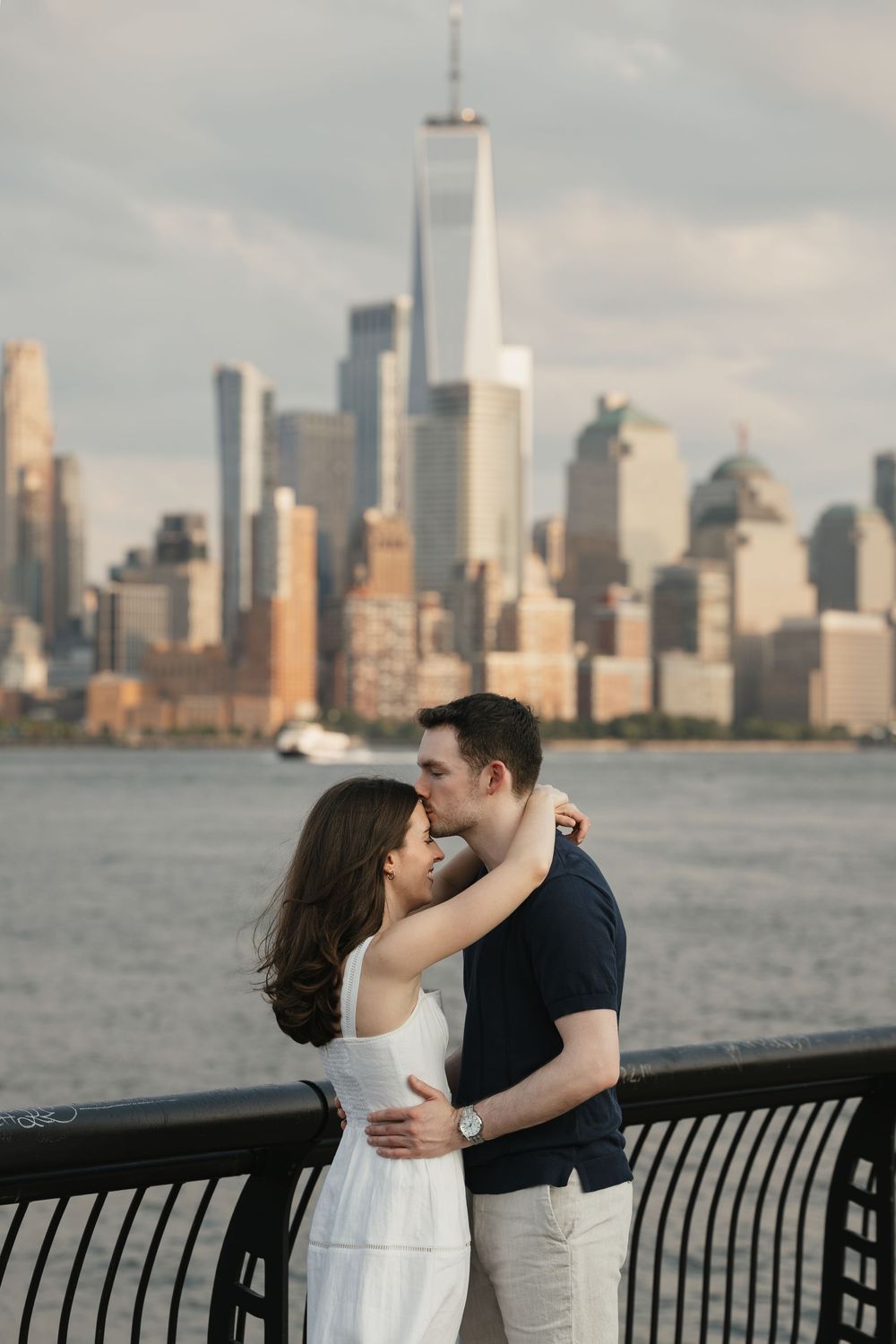 Couple sharing a romantic kiss with the NYC skyline and One World Trade Center in the background.