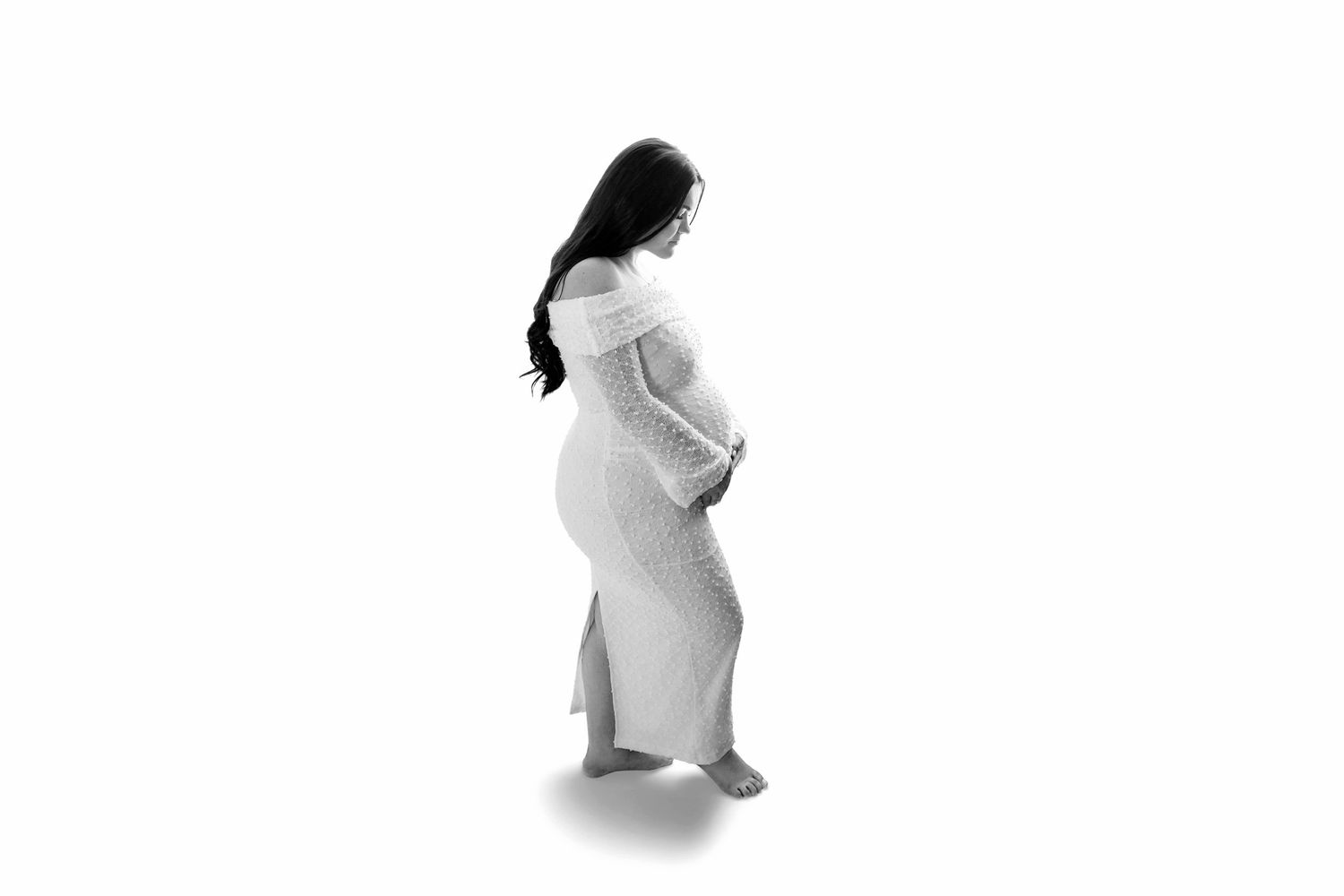 Black and white photo of a pregnant woman sitting with her toddler child, both smiling in a studio setting.