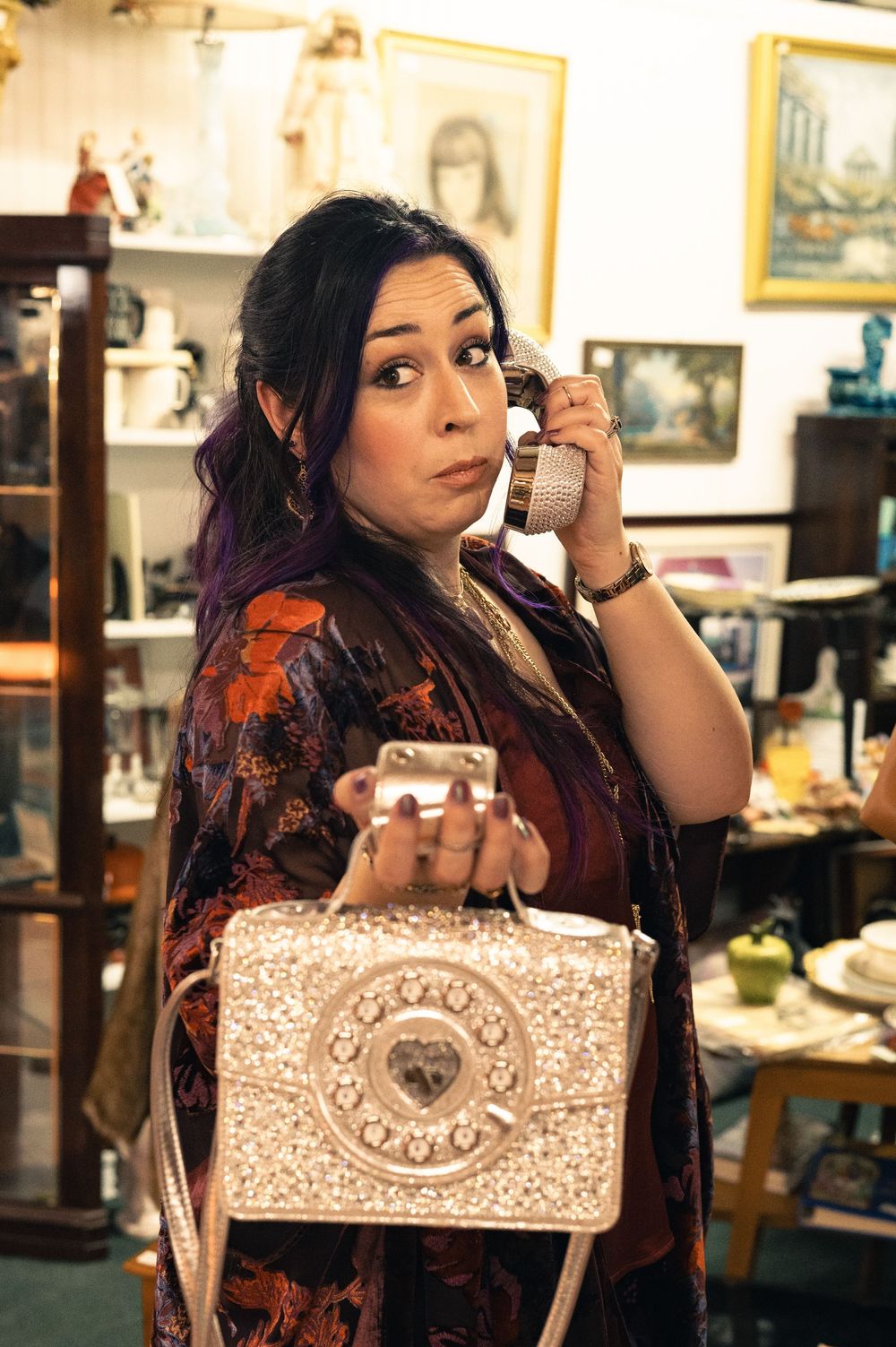 Woman holding vintage rotary phone handset and ornate beaded purse in an antique shop.