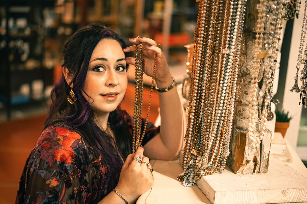 Woman browsing beaded necklaces in a boutique jewelry shop, wearing a floral dress.