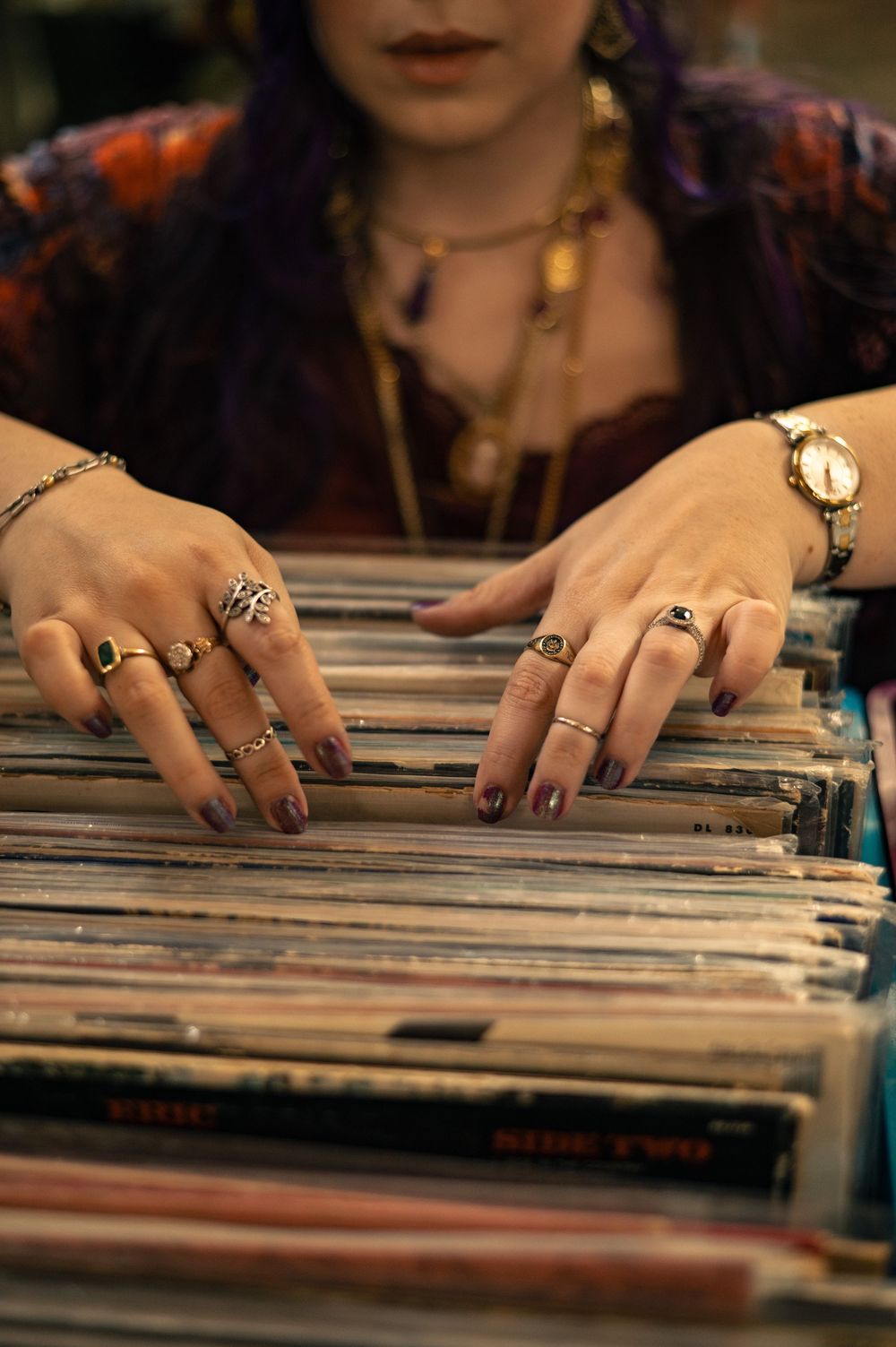Woman with purple hair and rings browses vinyl record collection in a music store.