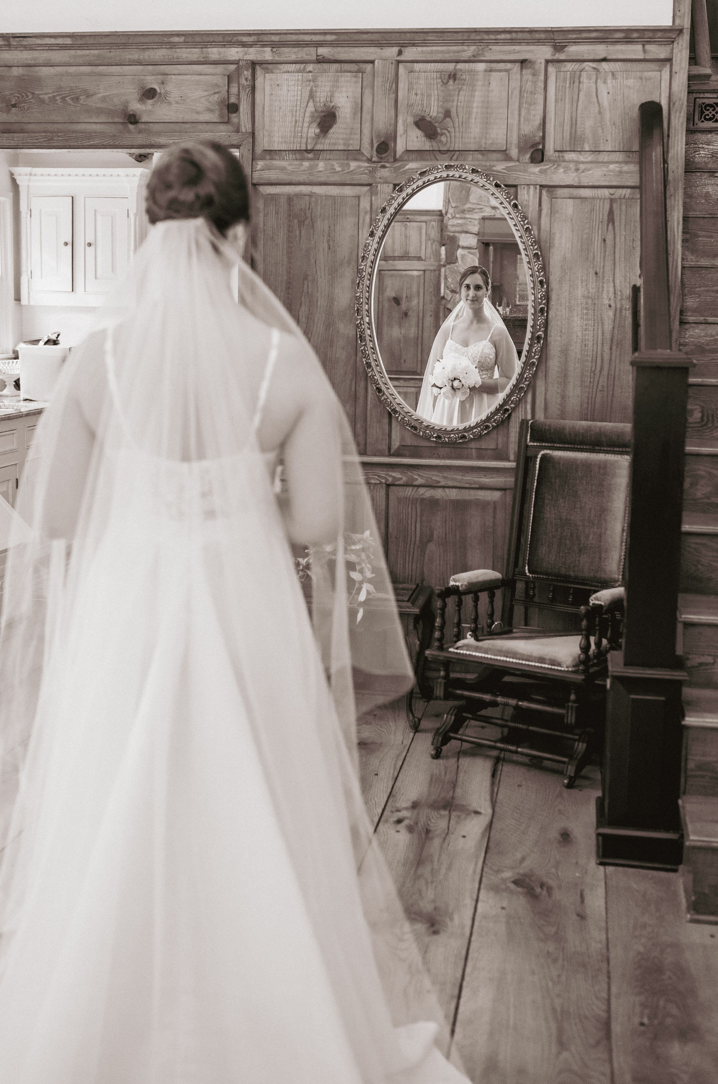 Bride in white gown and veil reflected in vintage oval mirror.