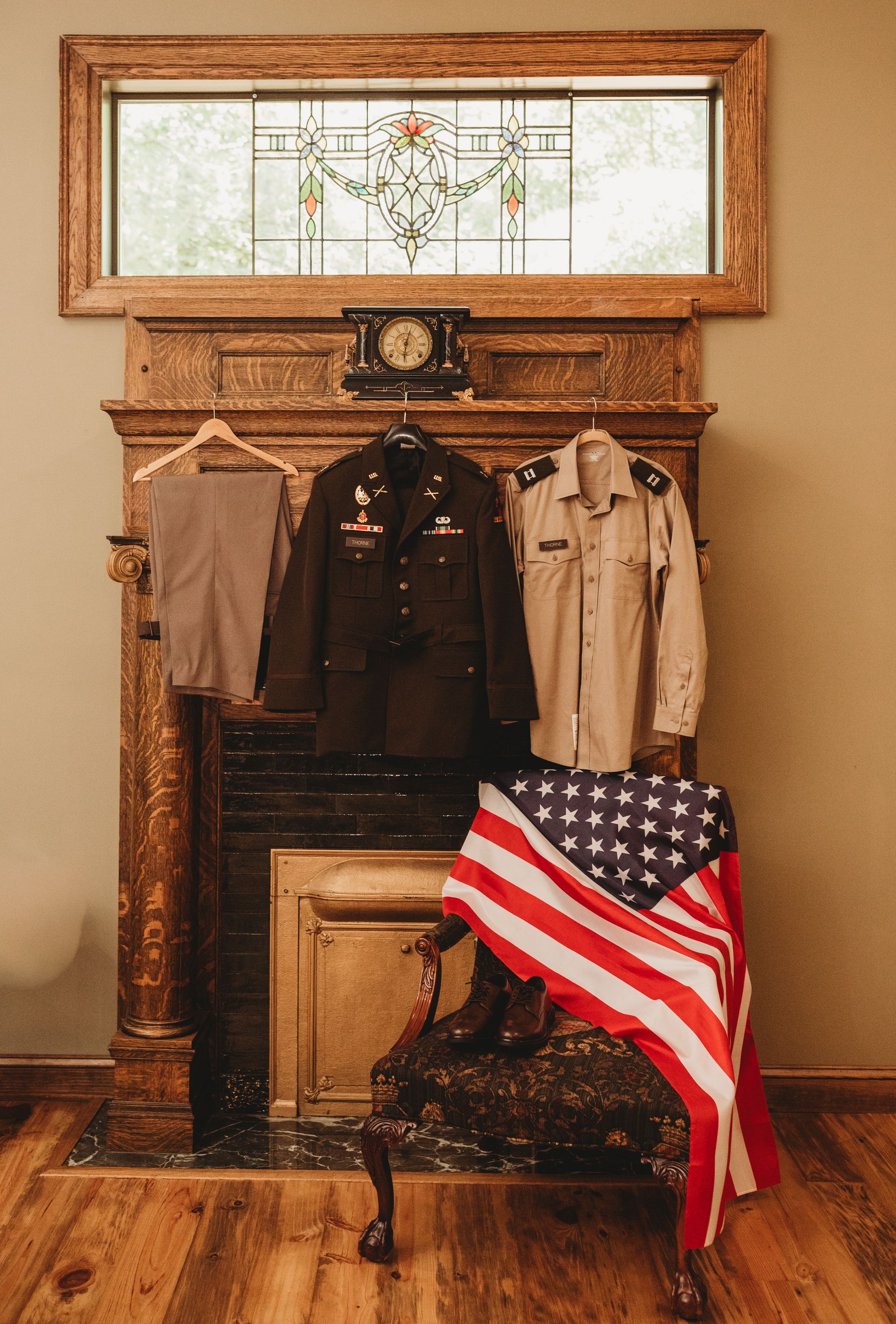 Military uniforms and American flag displayed on antique fireplace mantel with stained glass transom window.