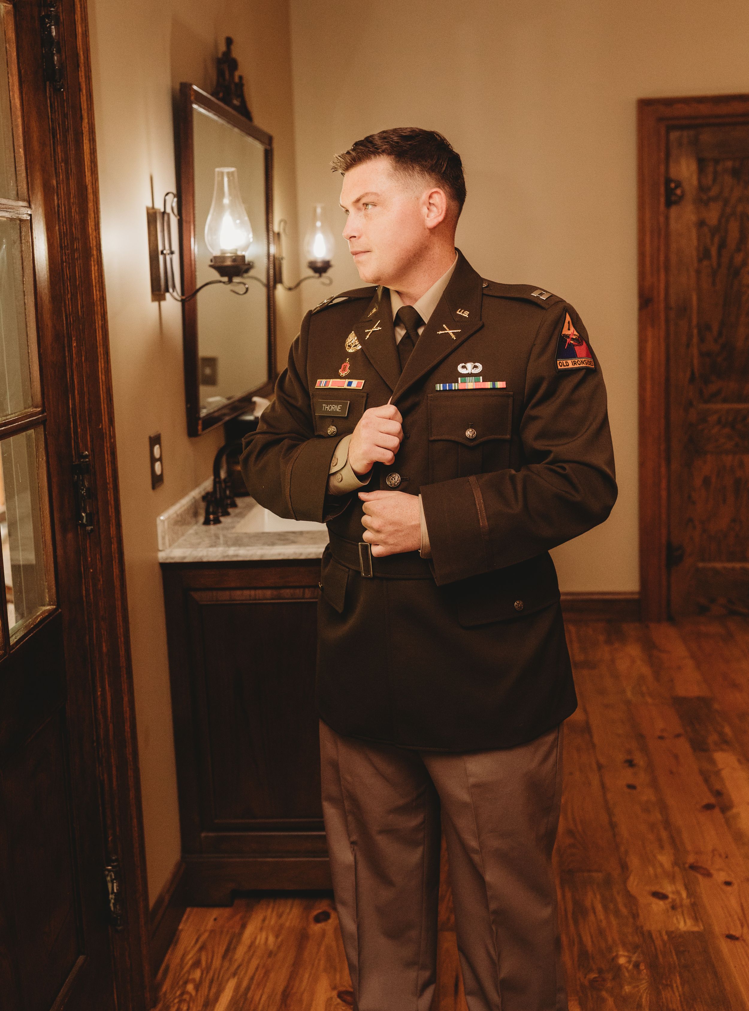 Military officer in dress uniform adjusting jacket indoors with warm lighting.