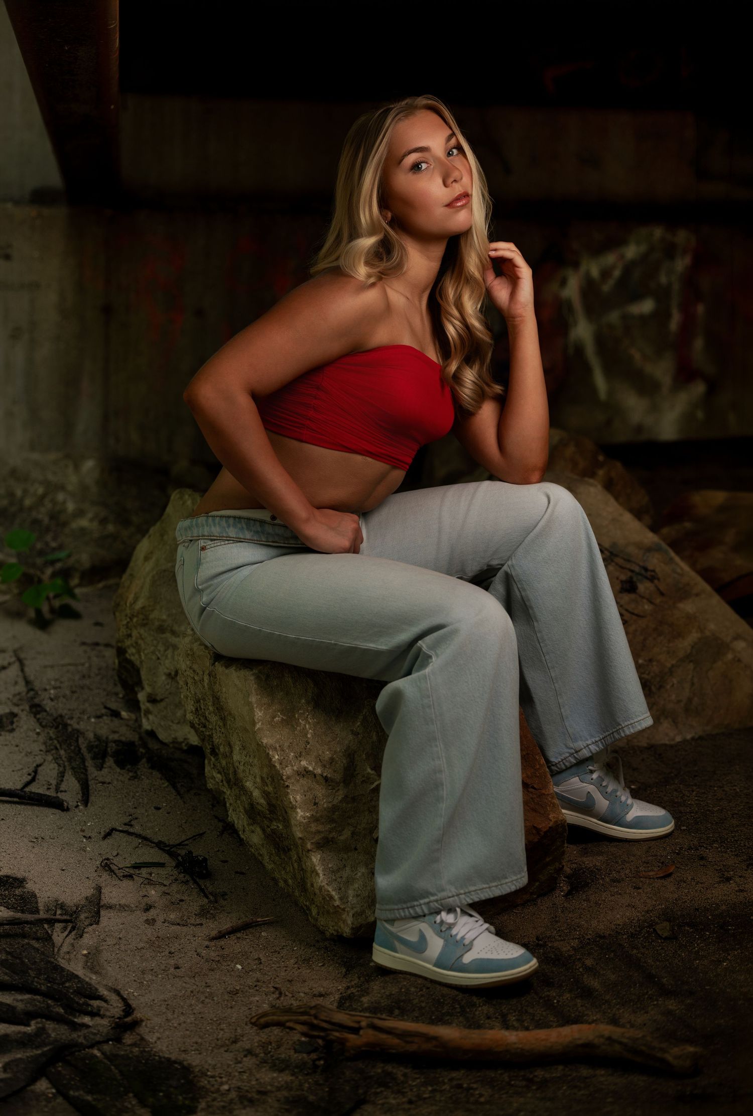 Senior portrait of a blonde girl in a red top and light pants in a rustic location