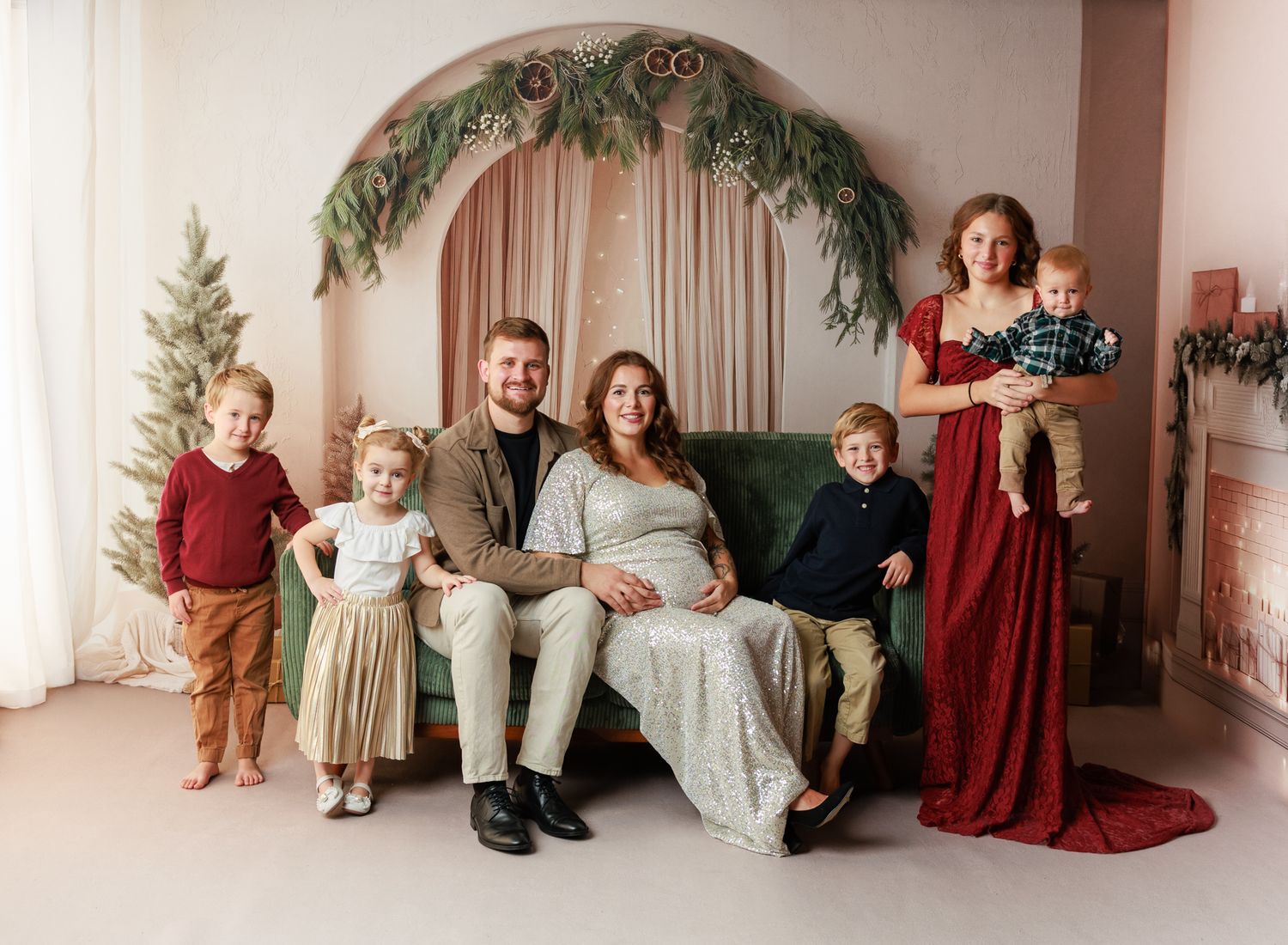 Family gathered on green blanket reading a book together near Christmas tree and fireplace in festive holiday setting.