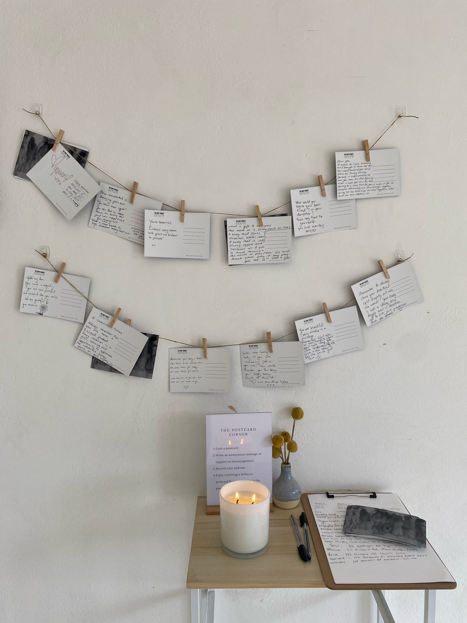 Index cards with handwritten notes clipped to string garland above a small table with candle, vase, and guest book.