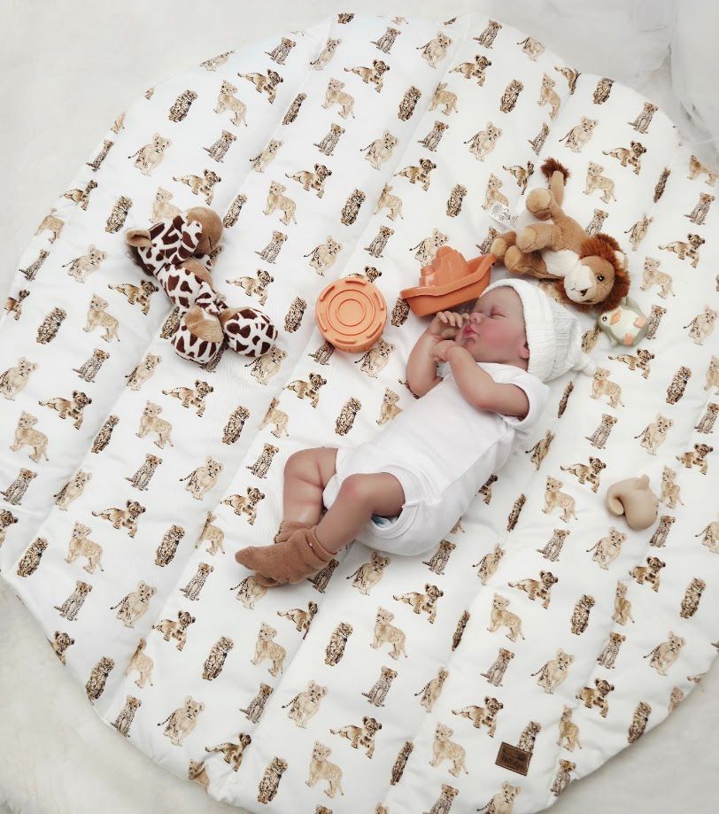 Newborn baby sleeping on white safari animal print play mat with giraffe and lion stuffed toys.