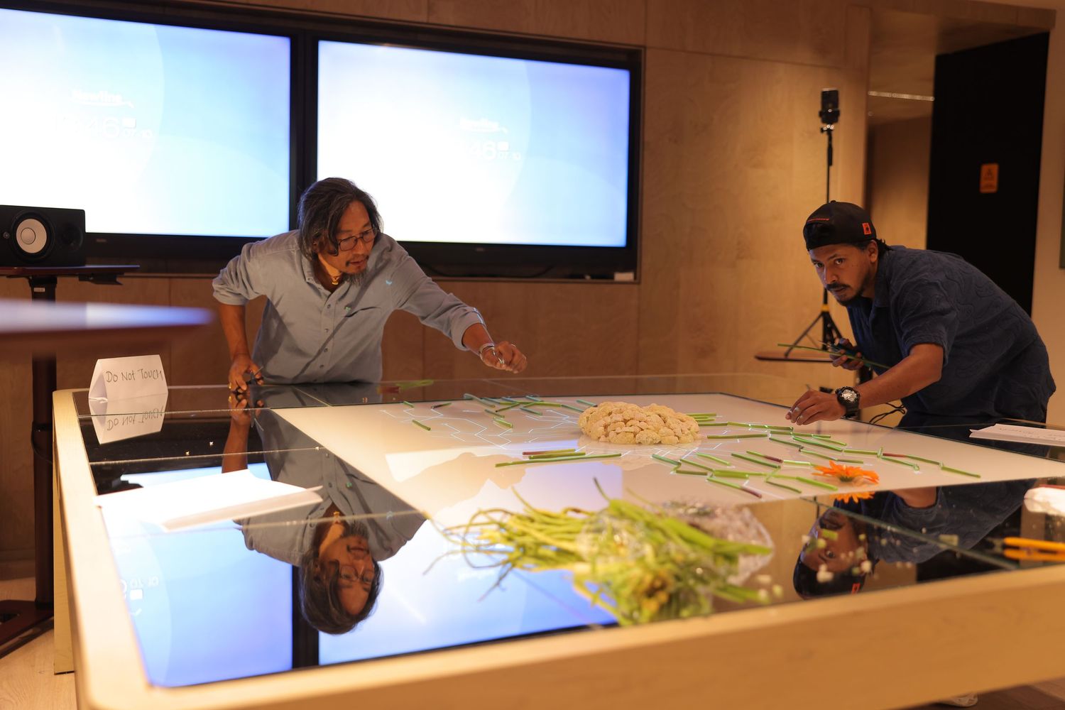 Two people collaborating over a large interactive touchscreen table displaying colorful digital content in a modern tech lab.