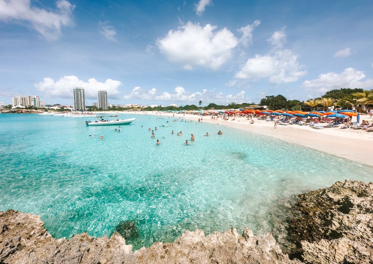 KLM Boeing airplane flying low over crowded Maho Beach in Sint Maarten during landing approach.