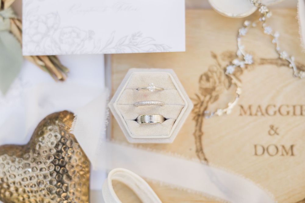 Wedding rings in a hexagonal velvet box beside personalized wooden keepsake engraved with Maggie and Dom.