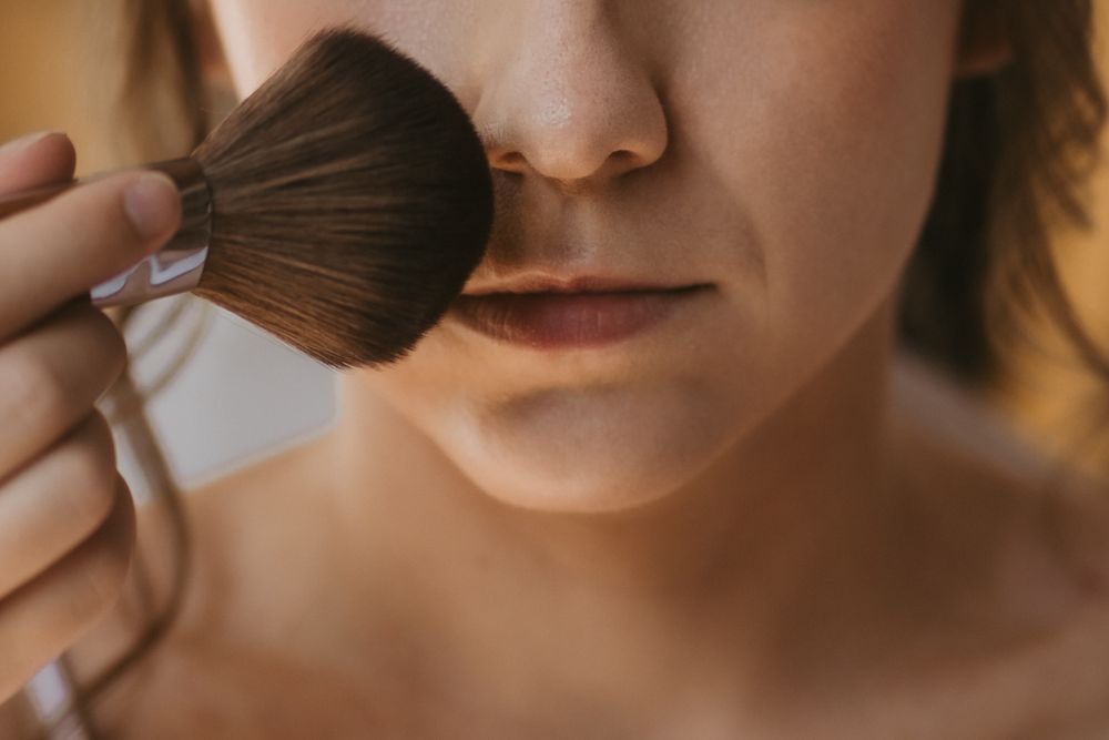 Woman applying powder makeup to her face with a large fluffy brush for a flawless complexion.