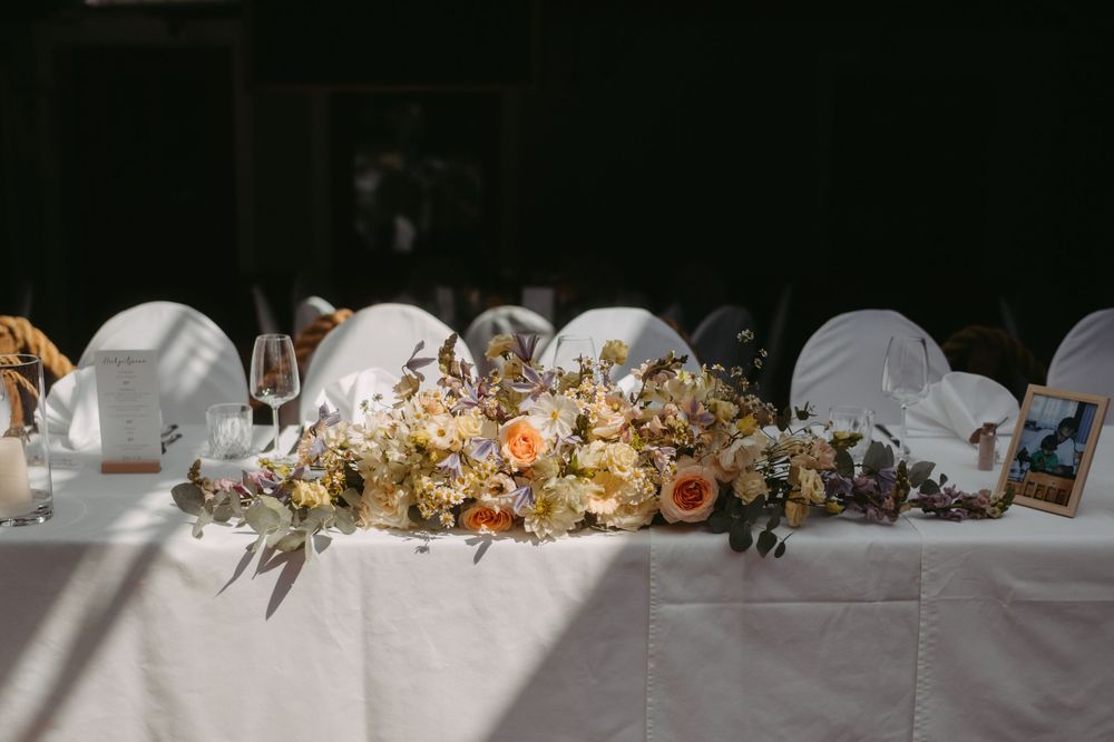 Elegant wedding head table with lush floral centerpiece featuring peach roses and wildflowers on white linen.