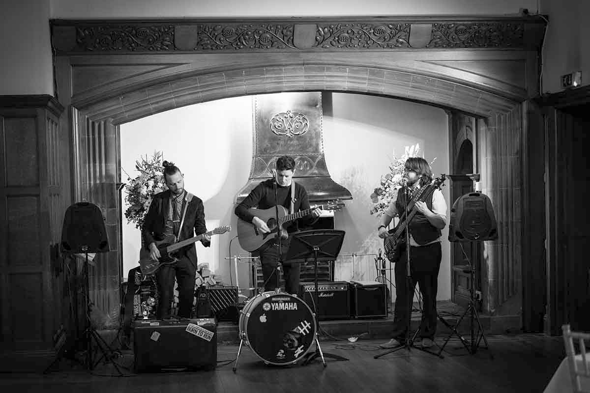 Black and white photo of a three-piece band performing on stage with guitars and a Yamaha drum kit.