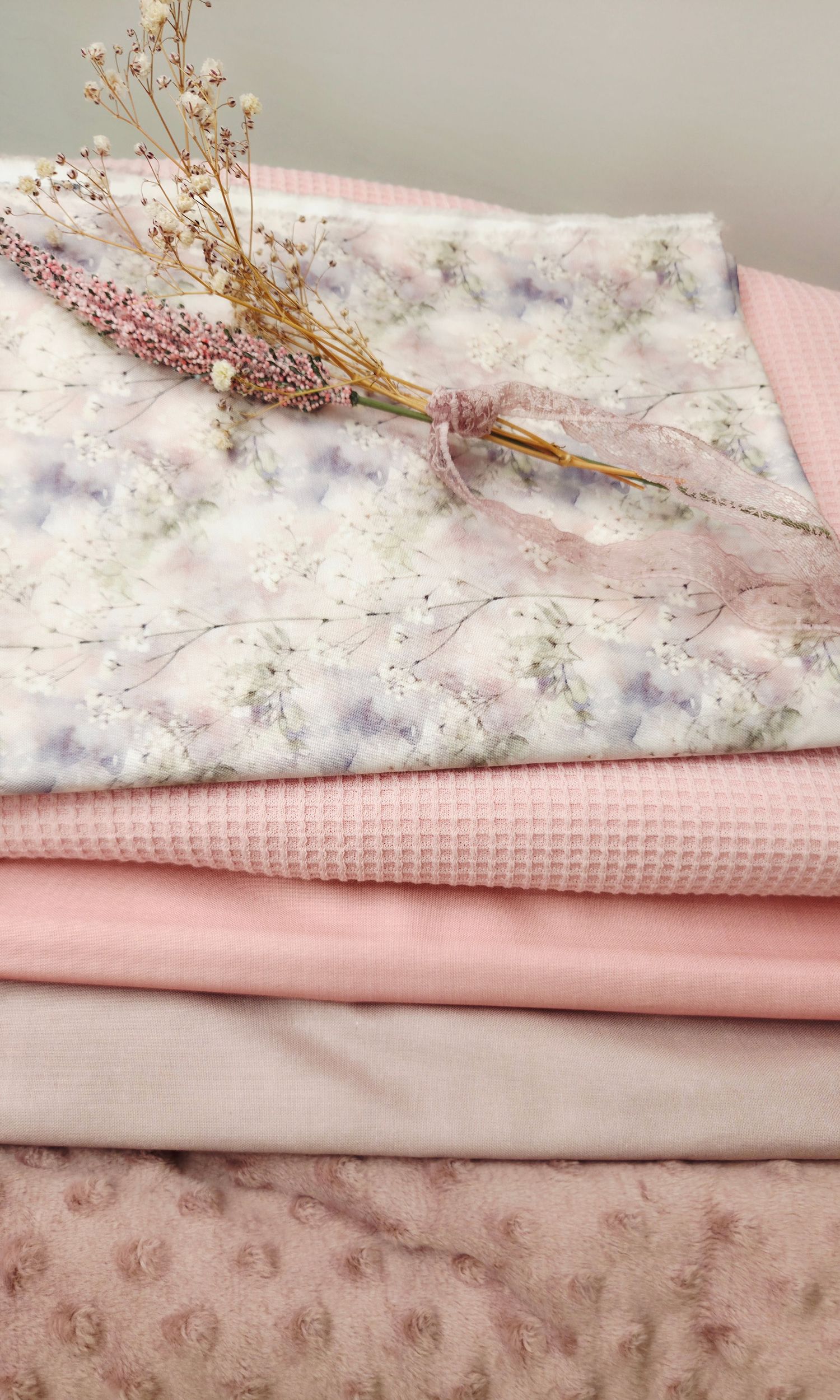 Stack of pink fabrics with floral print, waffle knit, and minky textures, topped with dried lavender bouquet.