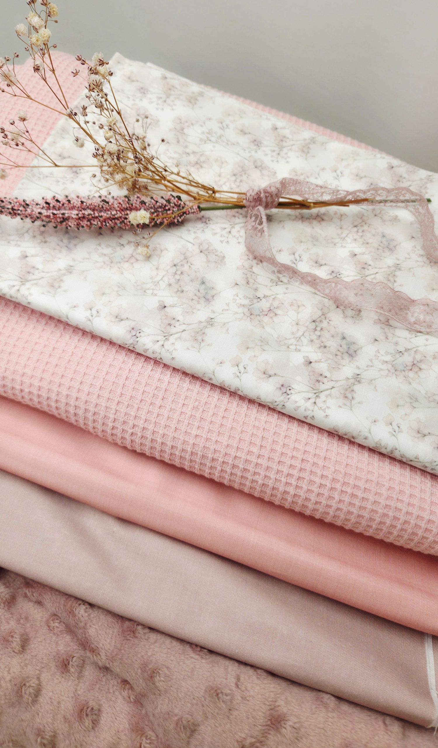 Neatly folded pink fabrics in various textures with dried floral stems on top.