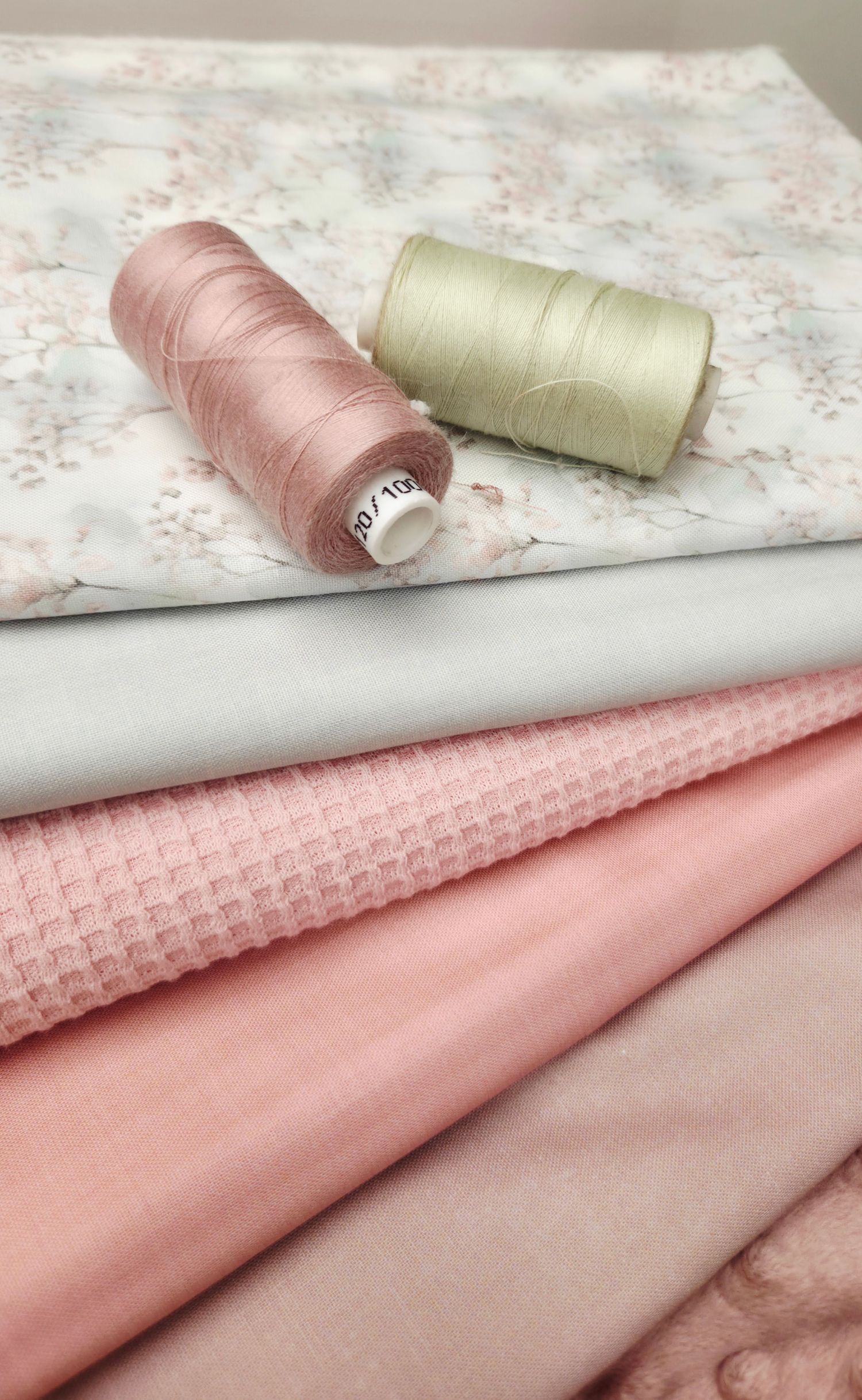 Pink and white fabric stack with waffle knit and floral print, paired with two spools of thread.