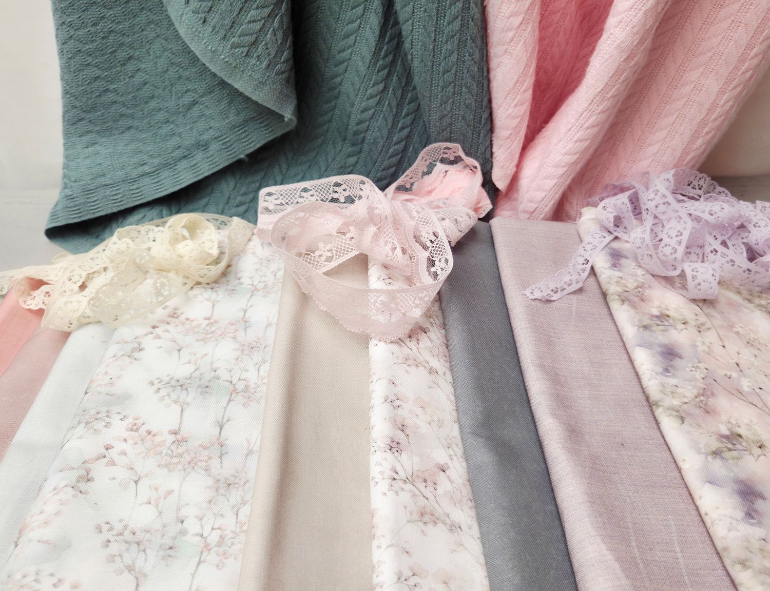 Soft pastel fabric swatches in pink, green, and floral prints with delicate lace heart accent, perfect for quilting and sewing projects.
