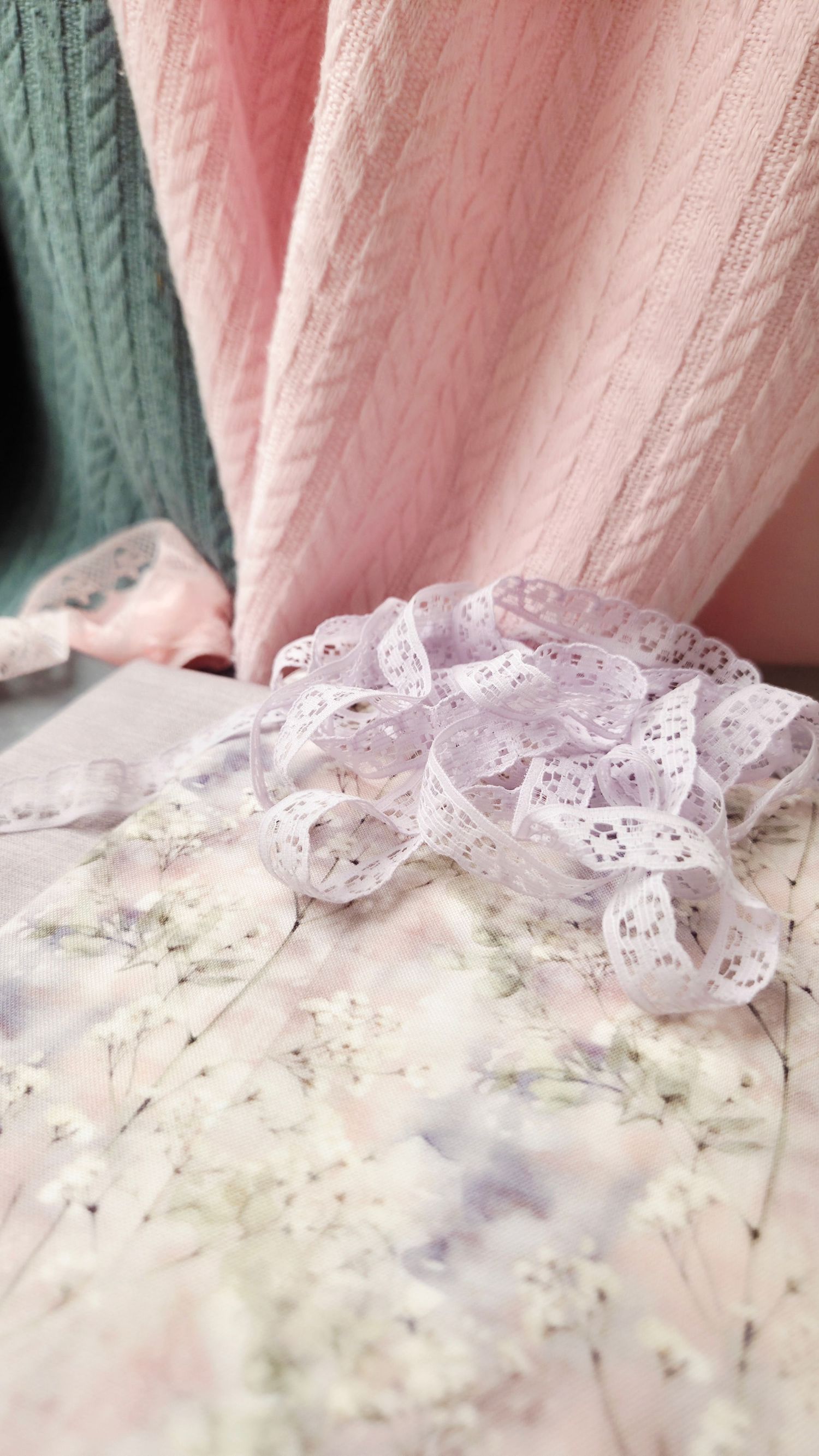 Delicate white lace ribbon and baby's breath flowers on a floral surface with soft pink knit fabric backdrop.