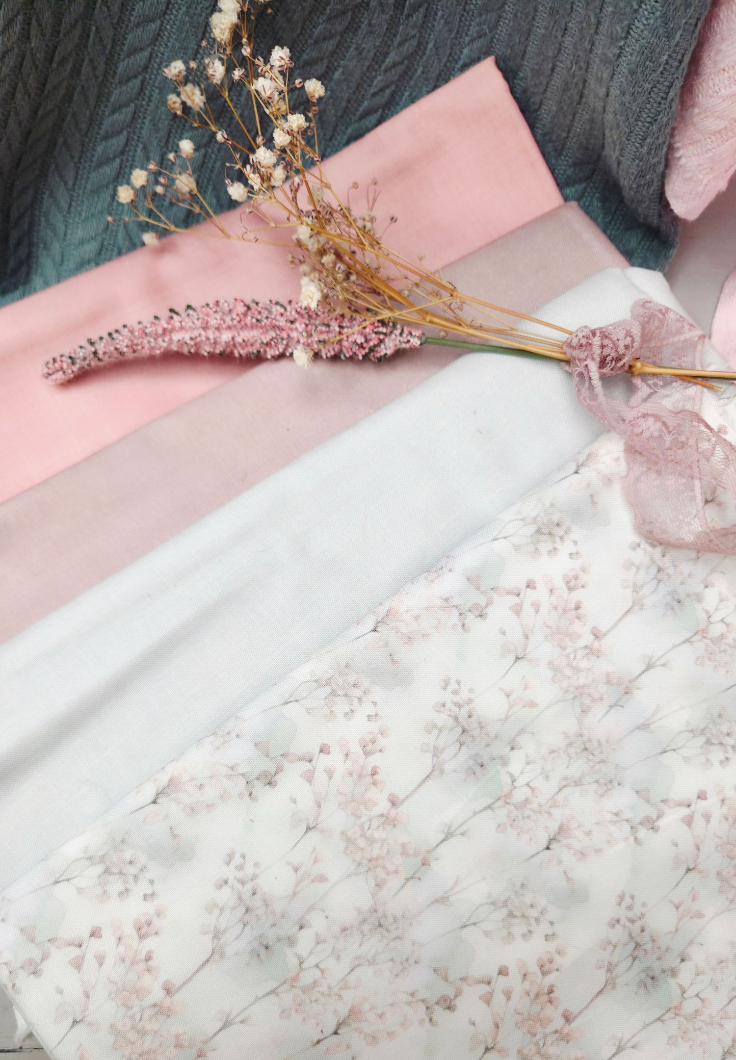Flat lay of pink fabric swatches, dried flowers, and floral chiffon arranged on a teal knit background.