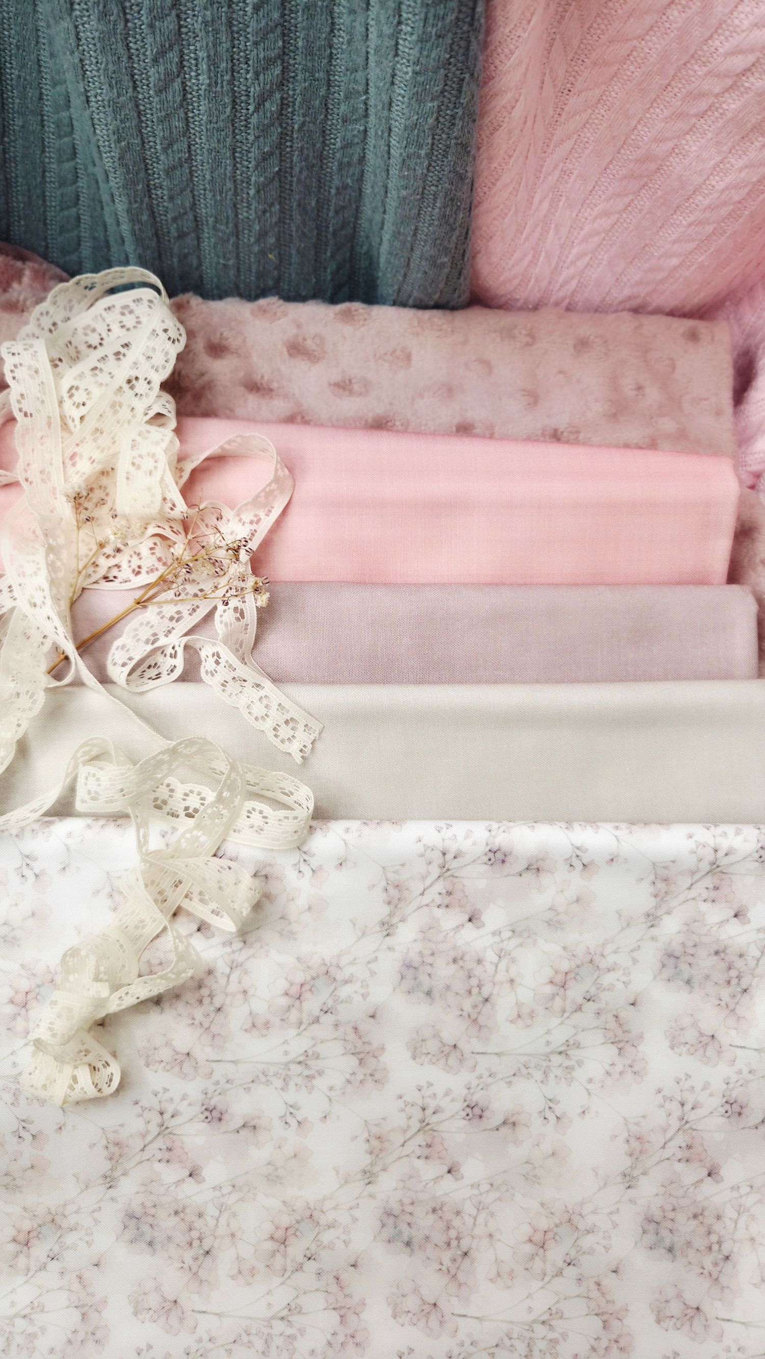 Soft pink and cream folded fabrics with delicate lace trim and floral patterns arranged in a romantic, feminine flat lay.
