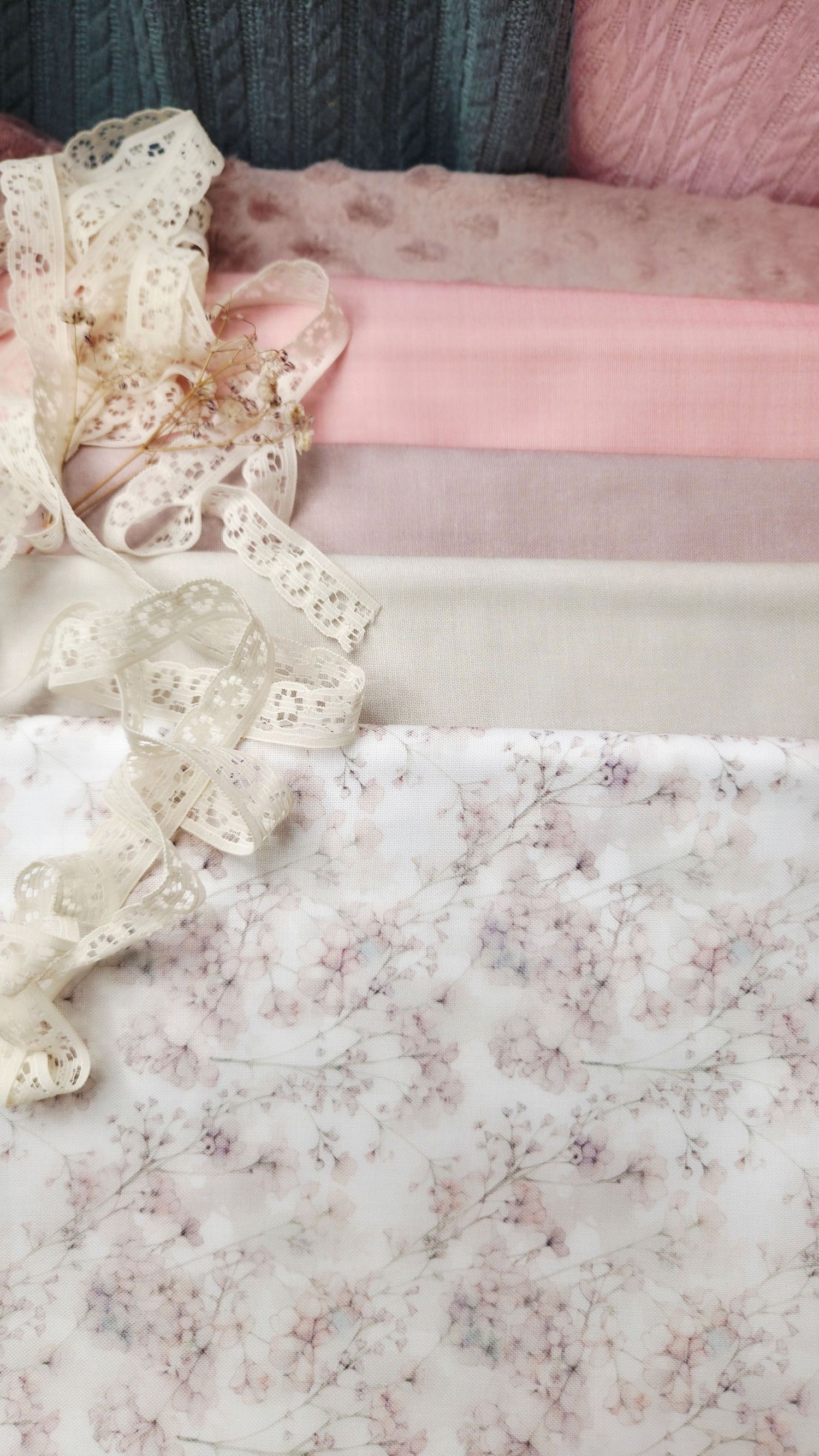Soft pink and cream fabric swatches with delicate floral print and ivory lace ribbon trim arranged in layers.