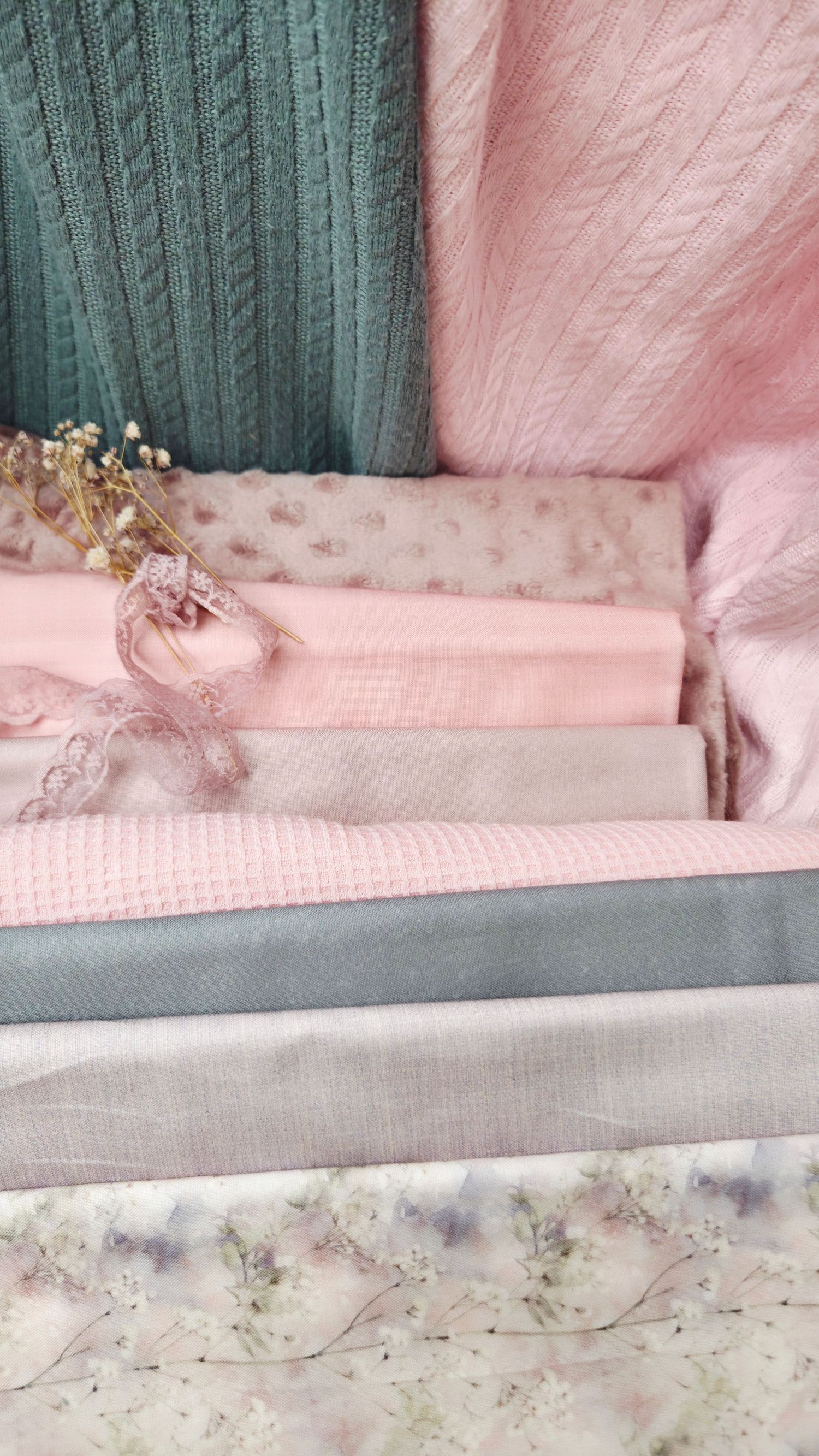 Soft pink and gray folded fabric swatches with dried flowers and lace ribbon, perfect for sewing or quilting projects.