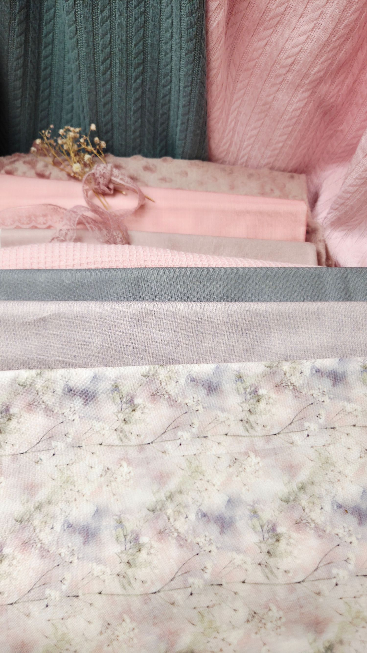 Layered fabric swatches in pink, gray, and floral print with delicate ribbon and dried flowers accent.