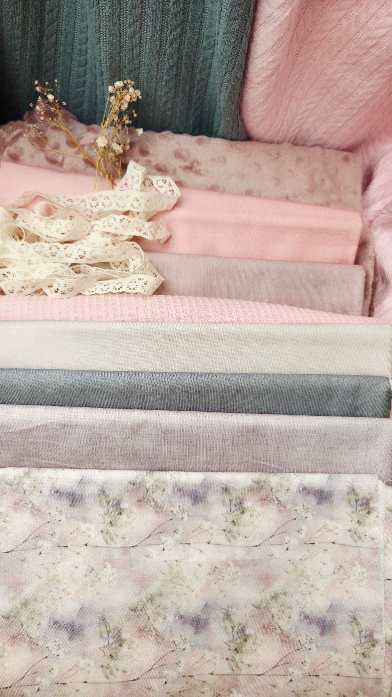Stacked pastel pink and gray fabric swatches with floral prints, lace ribbon, and dried flowers in a soft feminine arrangement.