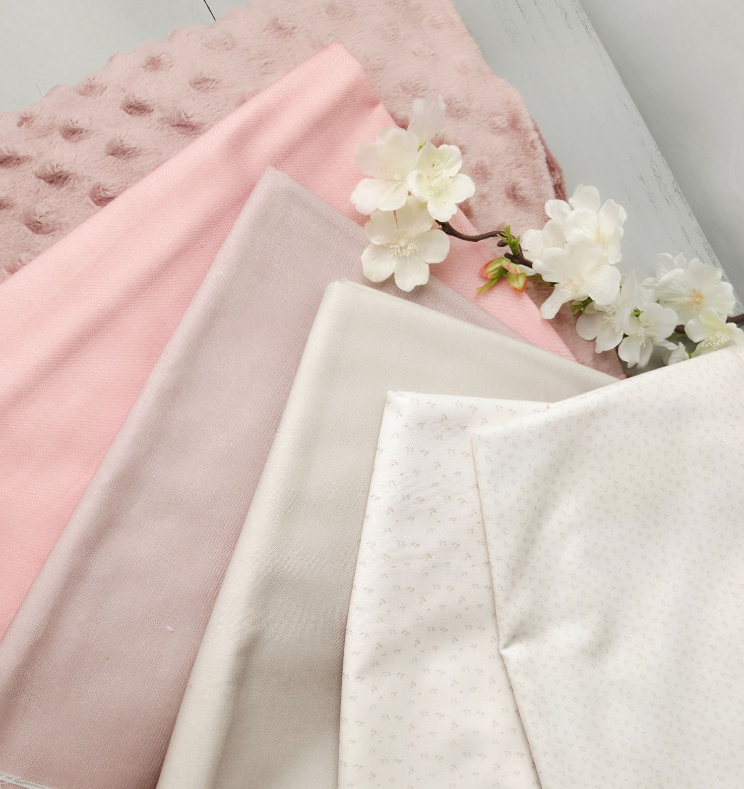 Soft pink and neutral fabric swatches arranged with white cherry blossoms, including minky dot, cotton, and dotted prints.