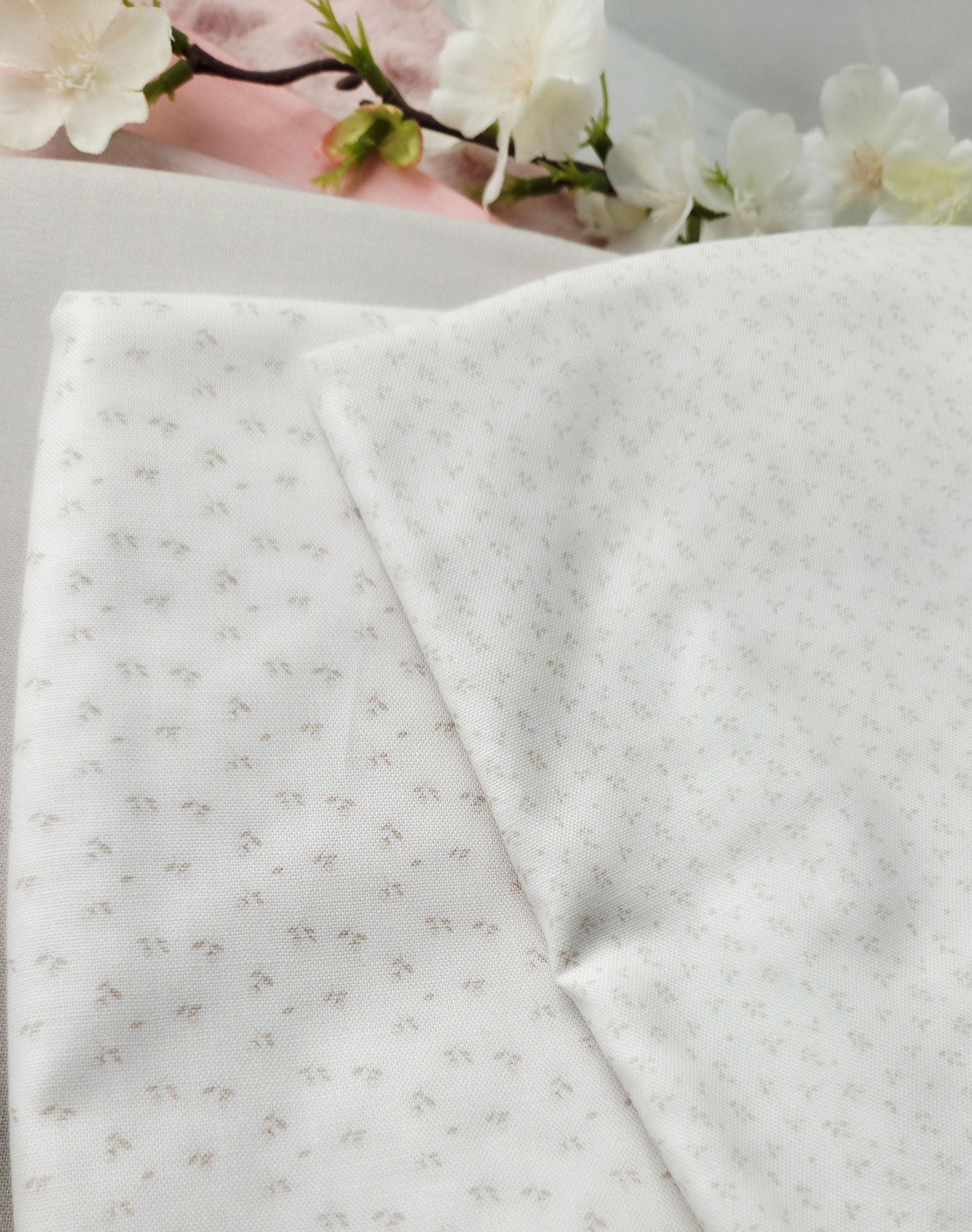 White fabric with delicate grey floral print pattern, displayed with cherry blossom flowers in background.